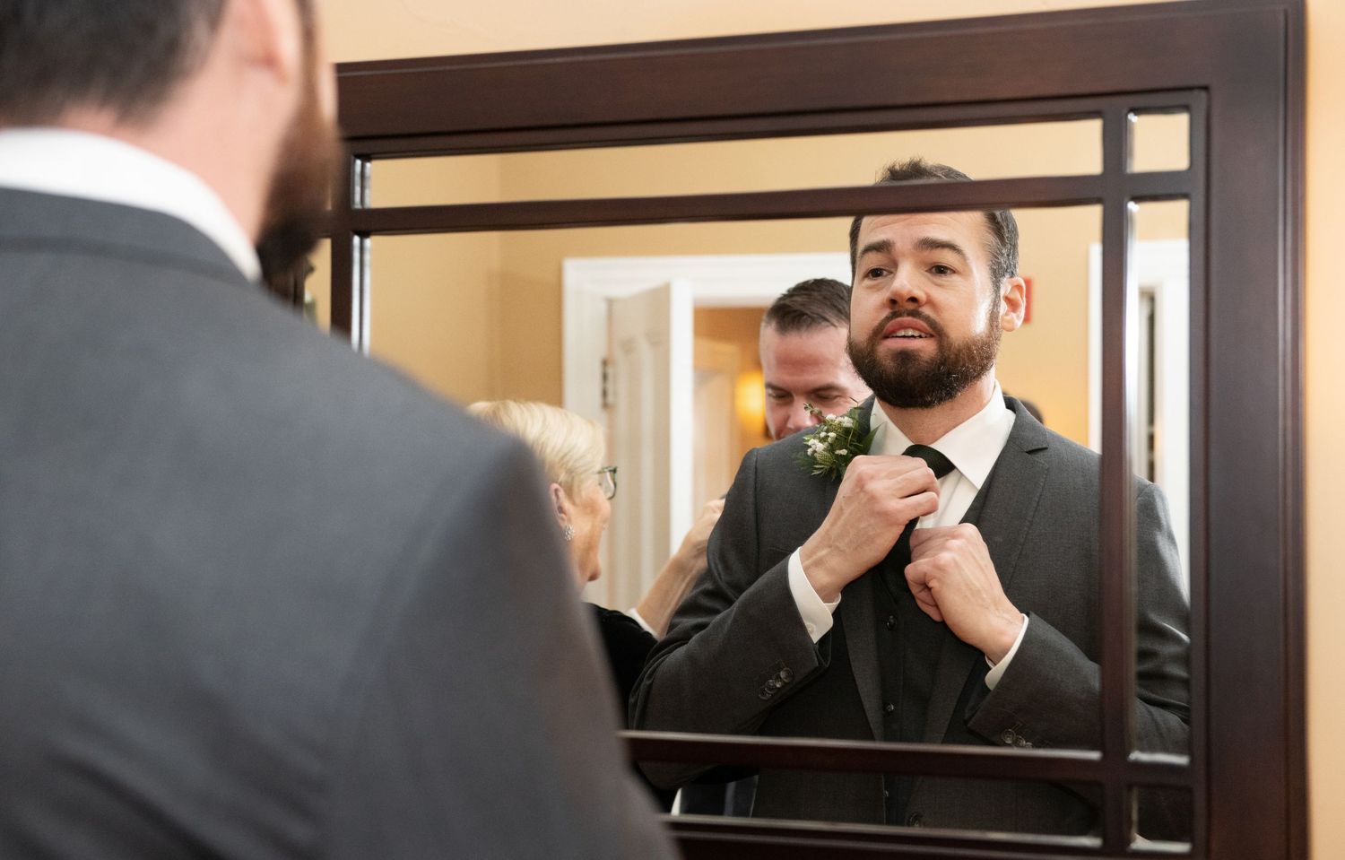 A person adjusts their tie while looking in a mirror at their reflection.