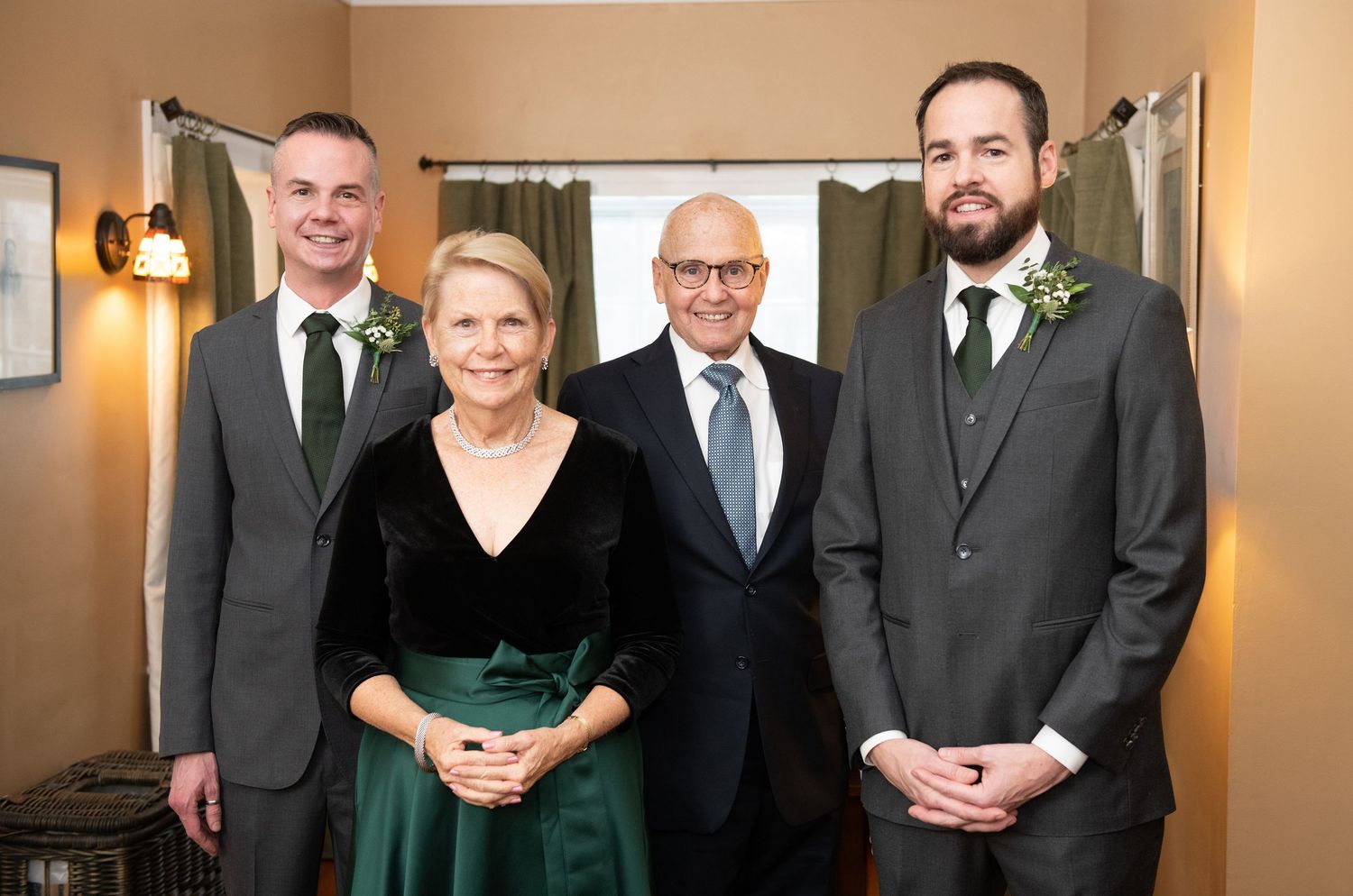 A group of formally dressed people stand together in an elegant hallway with warm lighting and beige walls.