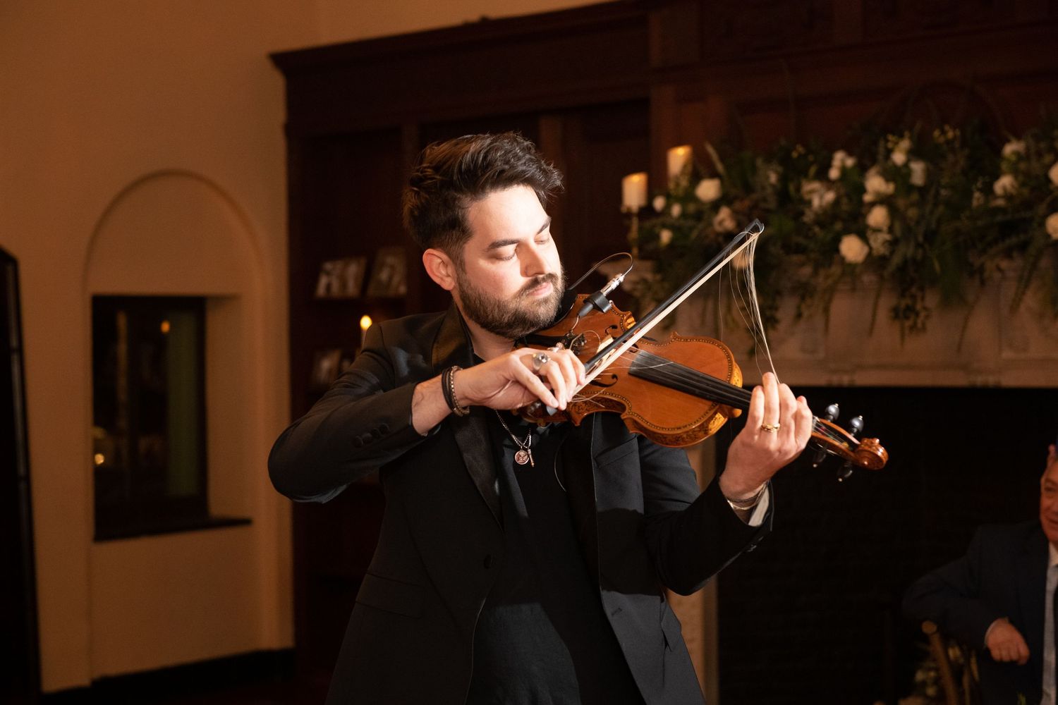A violinist performs on stage during a concert with dramatic lighting and ambiance in the background.