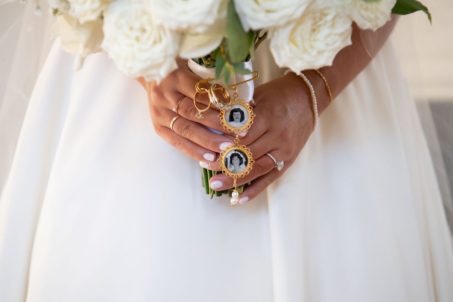 Close-up view of hands holding elegant white and cream wedding bouquets against formal dresses.