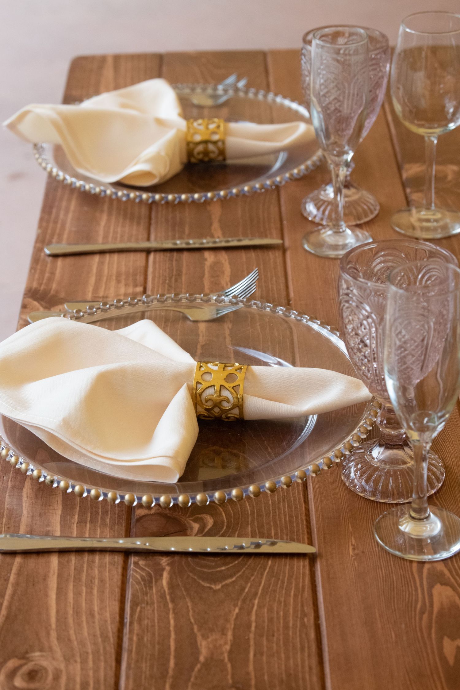 Elegant table settings with beaded charger plates and crystal glassware on wooden farmhouse tables.