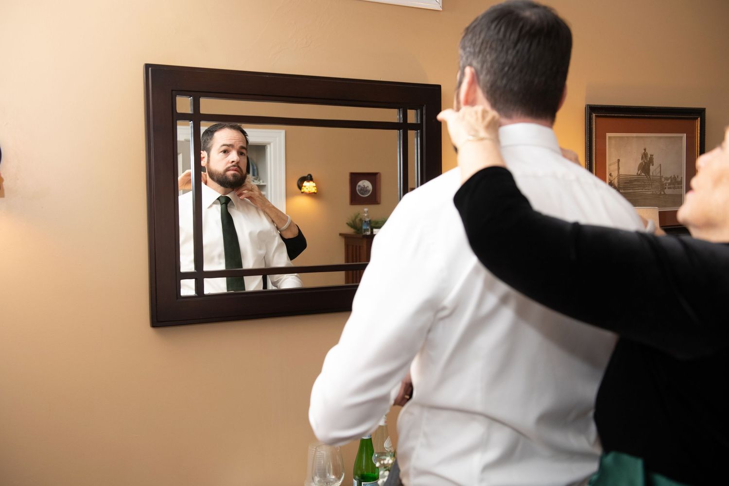 A person in a white shirt and black pants adjusts their tie while getting ready in a hotel room.