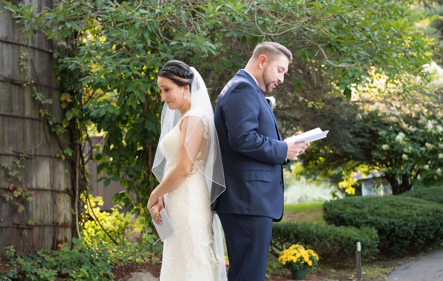 A first look wedding moment outdoors with the bride and groom standing back to back in a garden setting.
