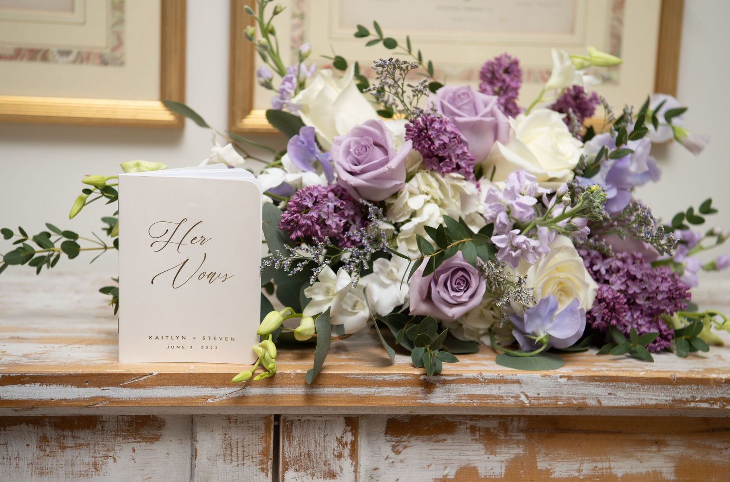 Elegant floral arrangement with purple and white roses next to a 'His & Hers' wedding sign on rustic wooden shelf.