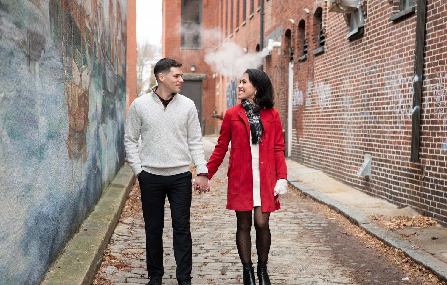 A couple walks together holding hands on a brick-lined alley during an engagement photo session.