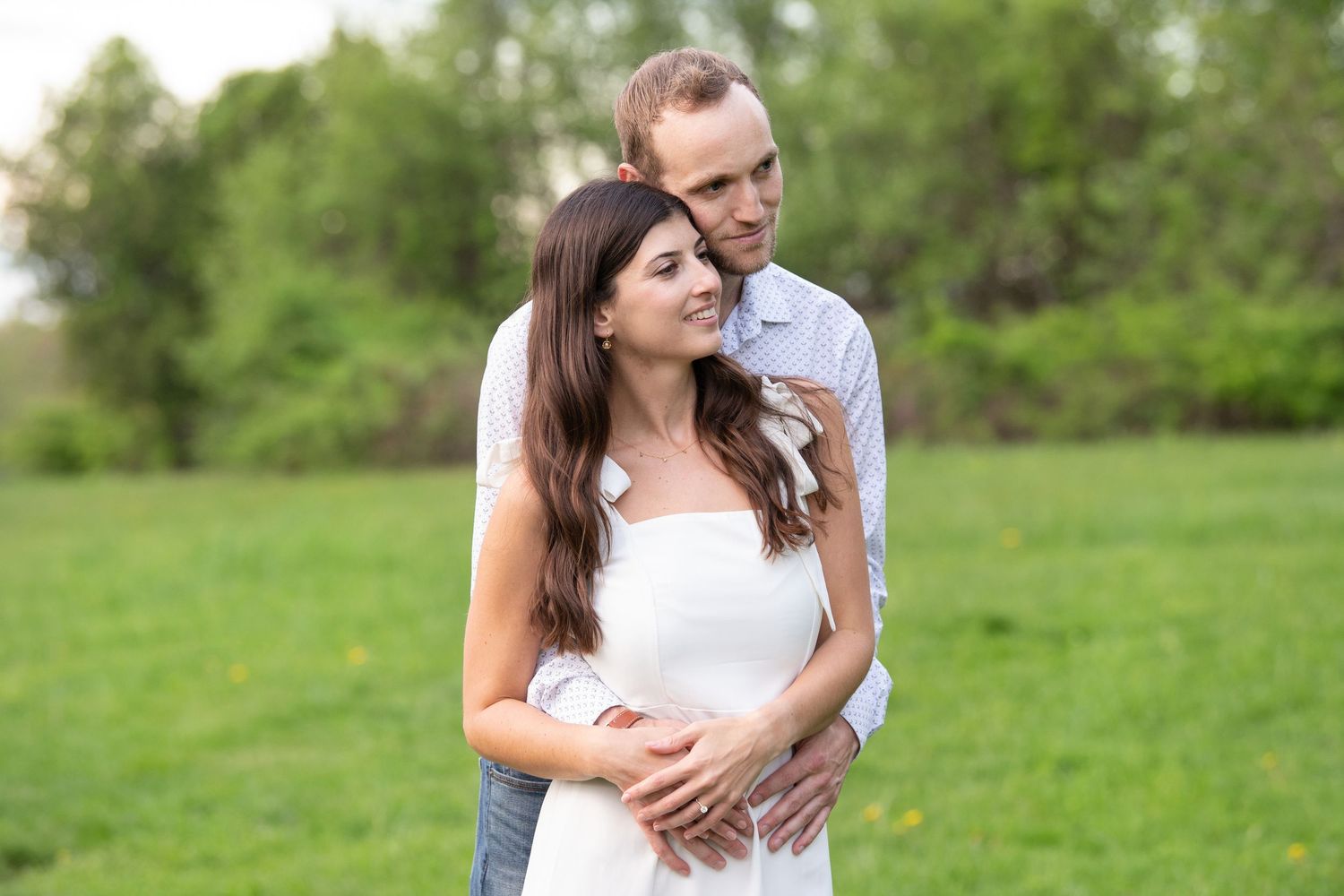 Romantic couple in a green meadow wearing white clothes embrace each other on a sunny summer day.