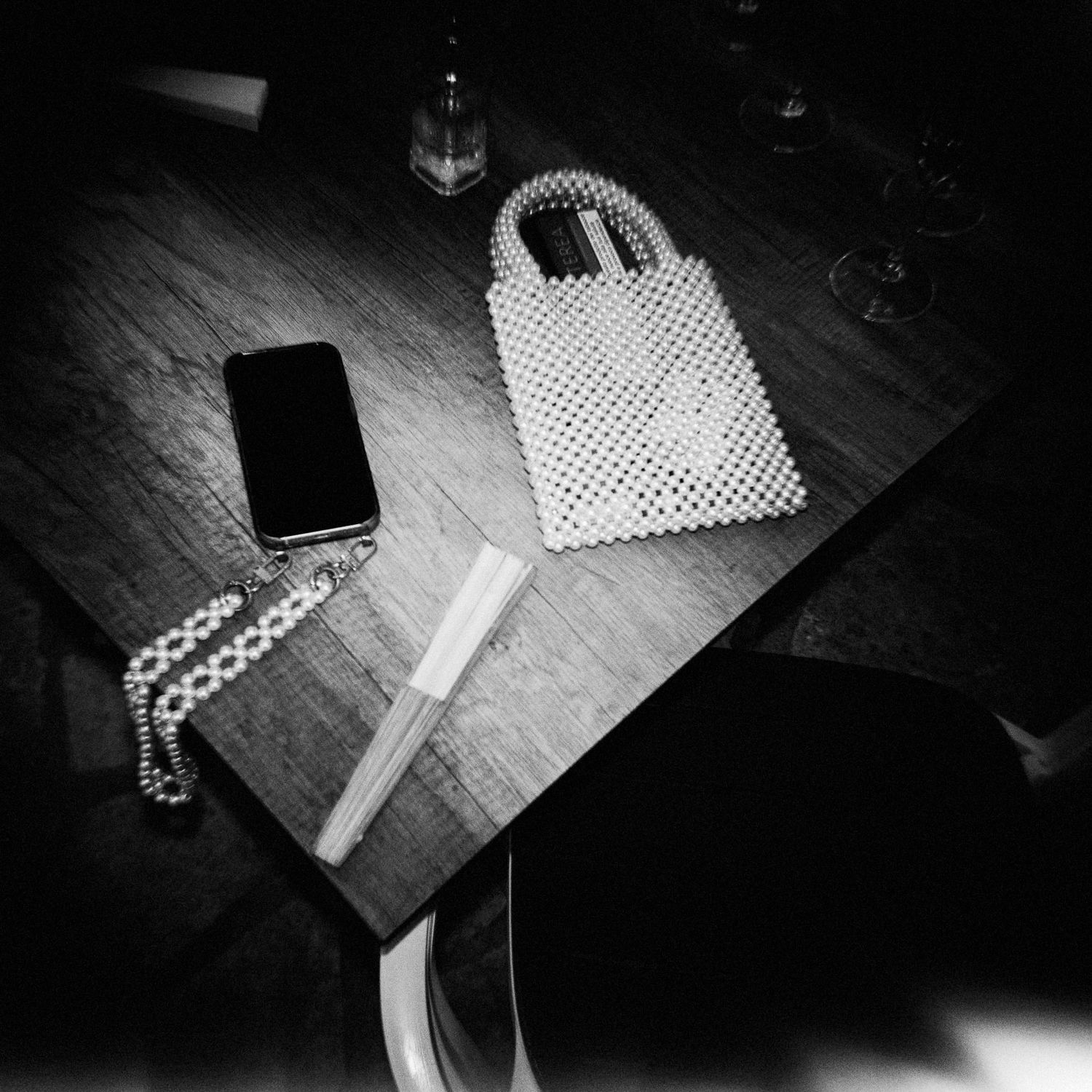 Black and white image of a phone, notebook, and polka dot bag arranged on a wooden surface.