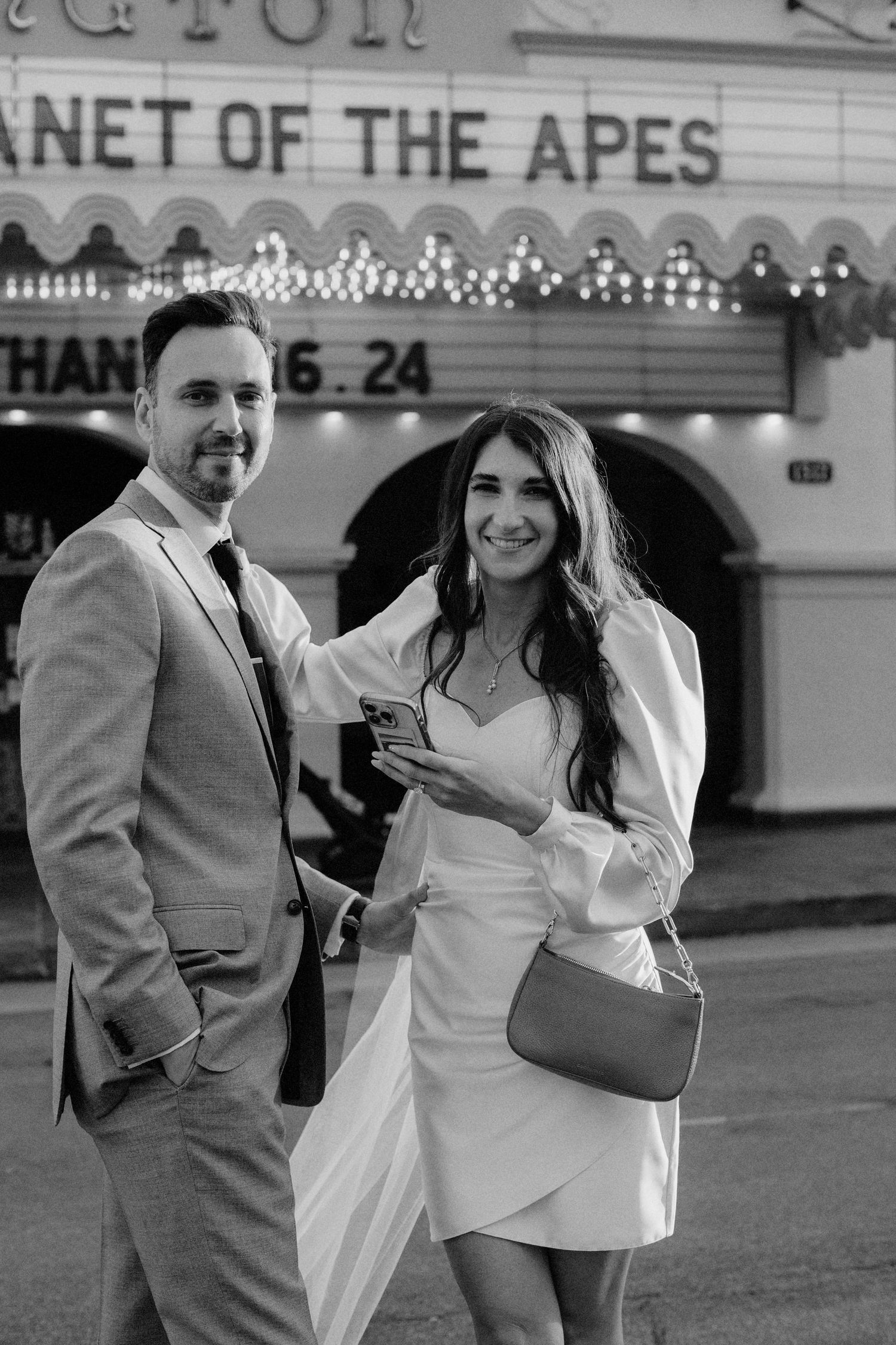 A couple shares a joyful moment in front of a vintage movie theater marquee sign at dusk.