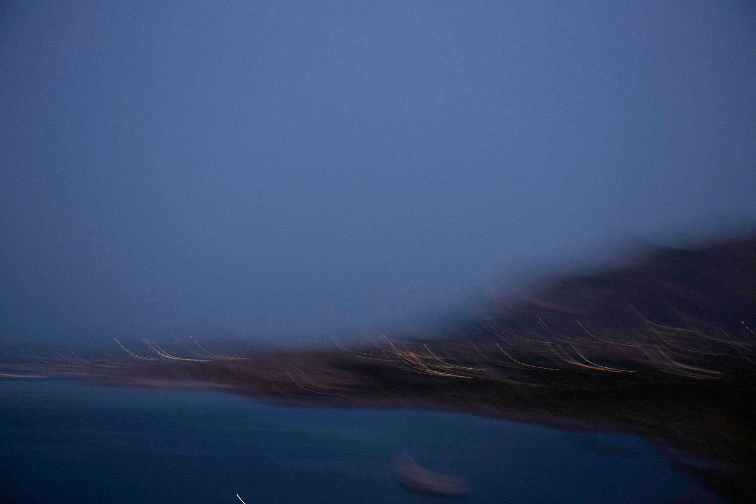 A moody twilight landscape shows dark mountains reflecting in still waters under a deep blue evening sky.