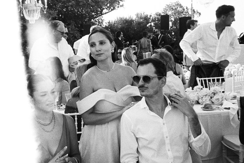 Black and white photo of elegantly dressed guests socializing at an outdoor wedding reception event.