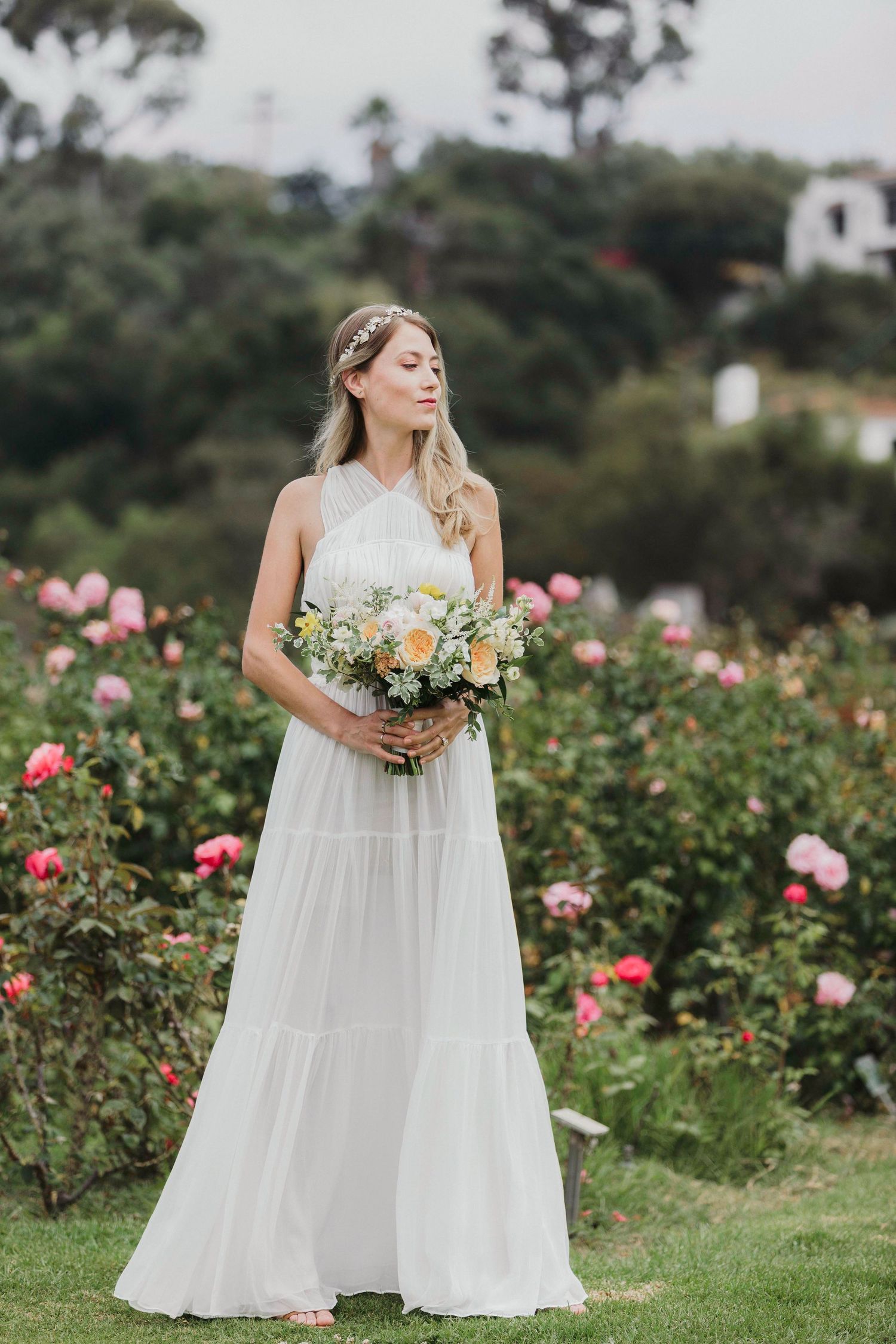 A flowing white dress is showcased against a backdrop of pink and peach roses in a garden setting.