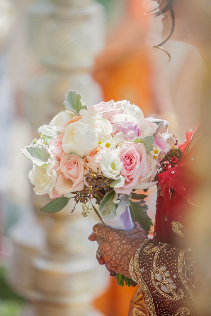 Bride holding a beautiful pastel wedding bouquet with pink and white roses, adorned with henna on her hands.