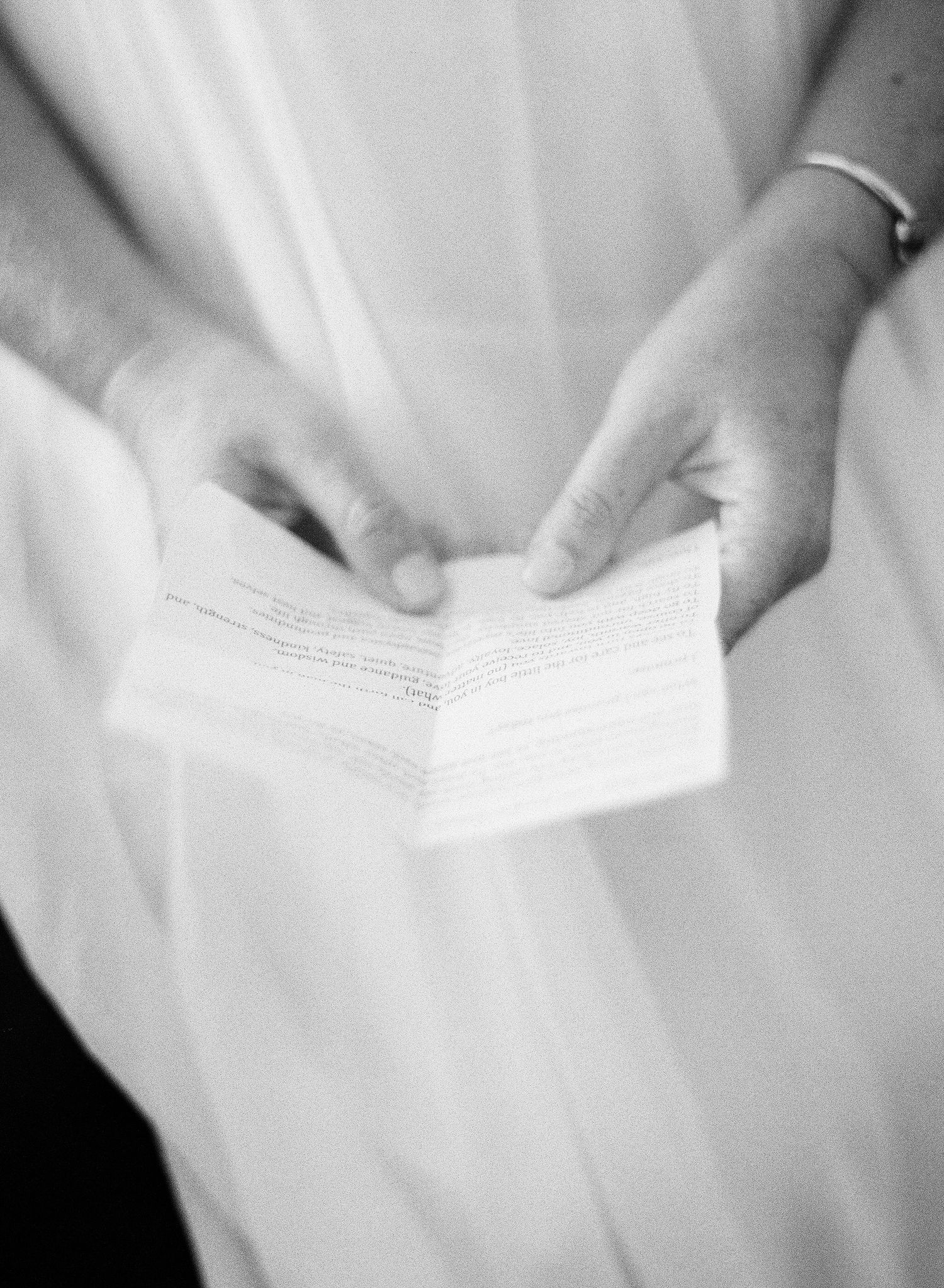 Hands holding a folded white paper note against a light fabric background in black and white photography.