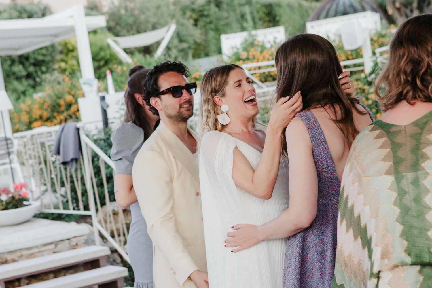 Wedding guests enjoying champagne toasts and celebrations on an outdoor patio during a sunny afternoon reception.