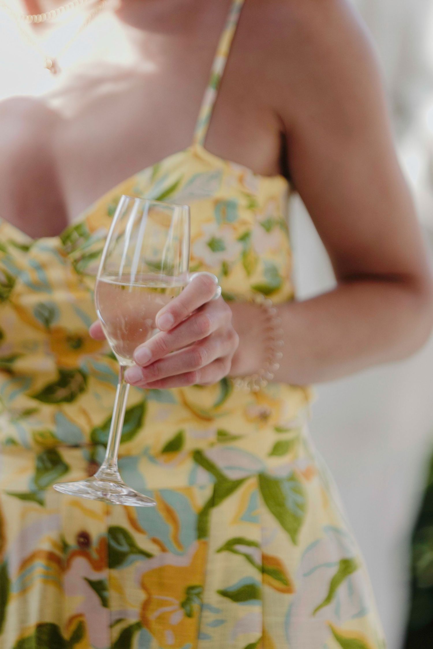 Person in yellow floral dress holding wine glass at outdoor event.