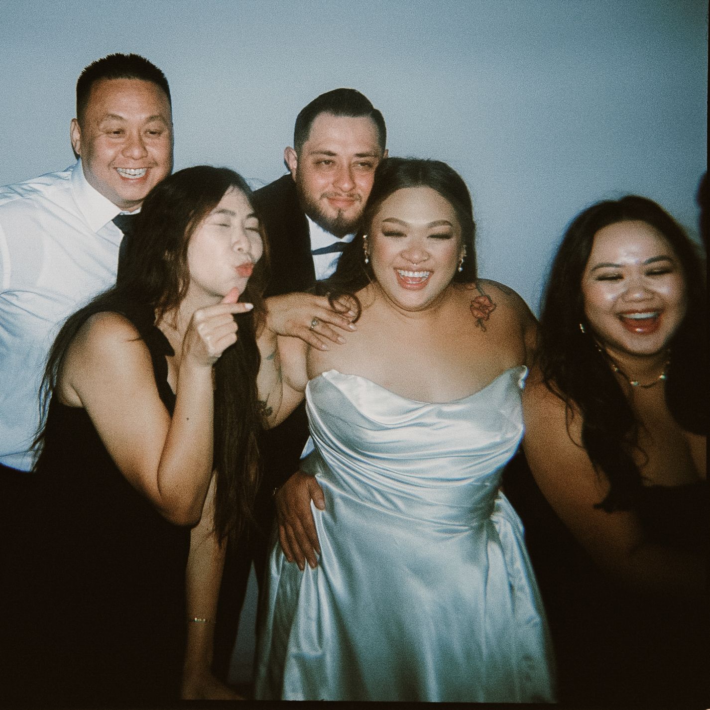 A group of friends pose together at a celebration, with one wearing a light blue formal dress in the center.