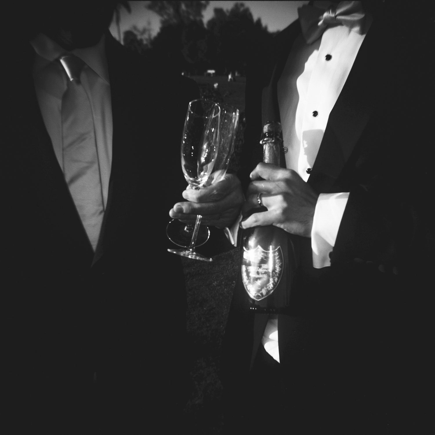 Black and white image of people in formal attire holding wine glasses and drinks at an elegant event.