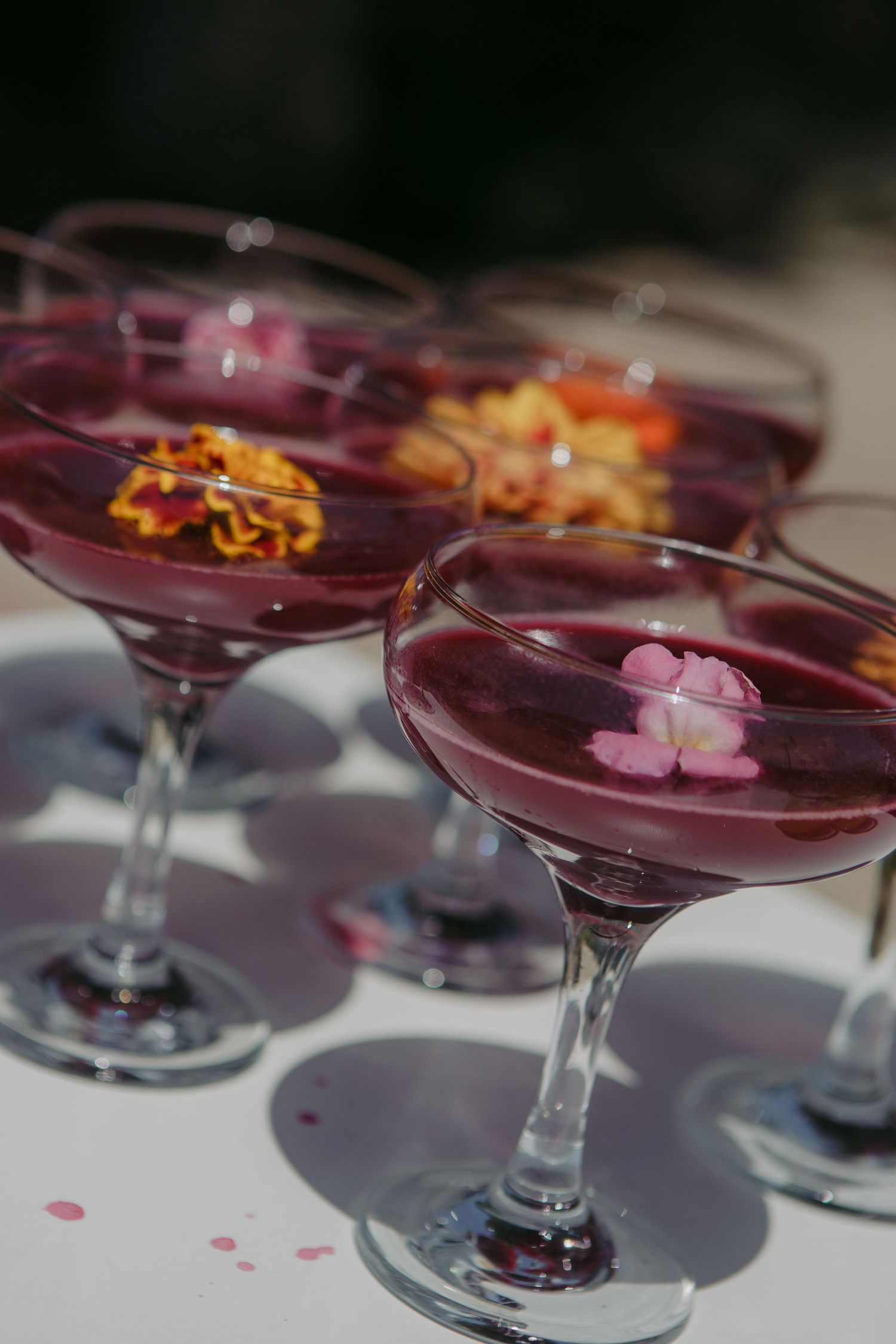 A row of elegant coupe glasses filled with purple cocktails garnished with orange zest on a light surface.