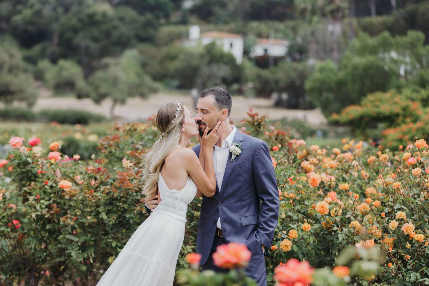 A tender moment between newlyweds surrounded by vibrant orange roses in a lush garden setting.