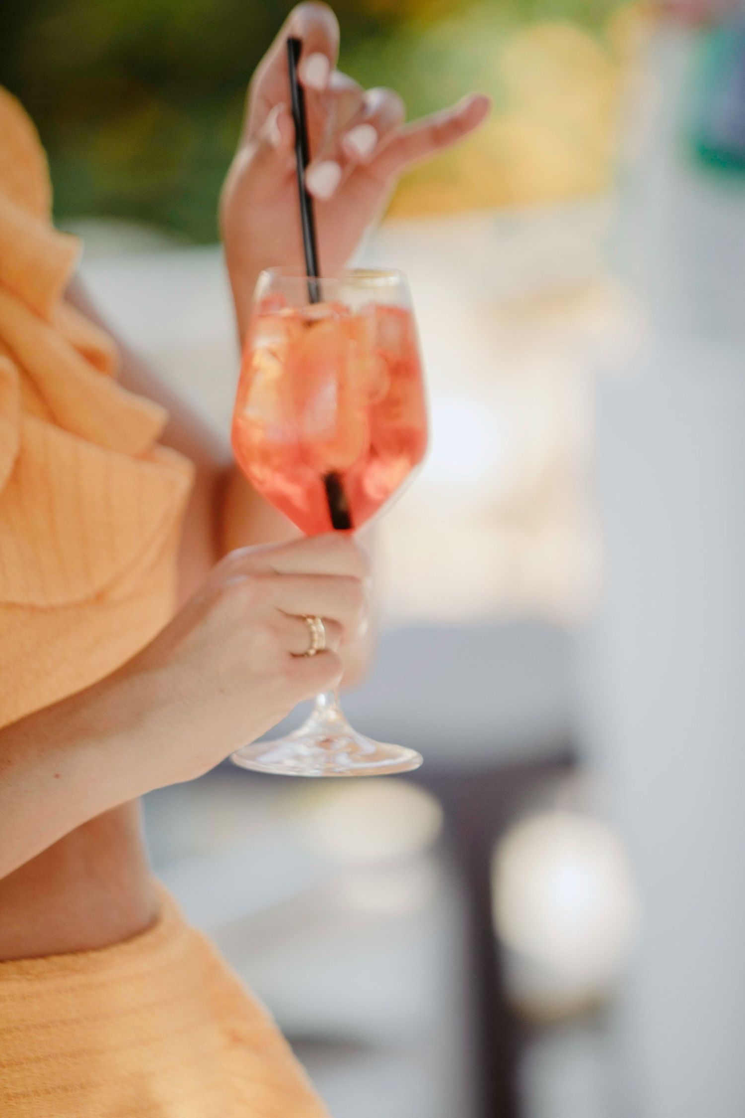 A close-up view of someone holding a wine glass with a blurred peachy background.