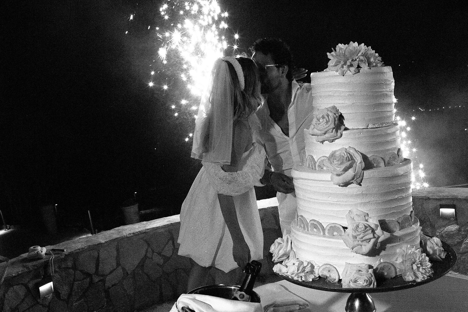 Black and white wedding cake cutting photo with sparklers creating a magical nighttime atmosphere.