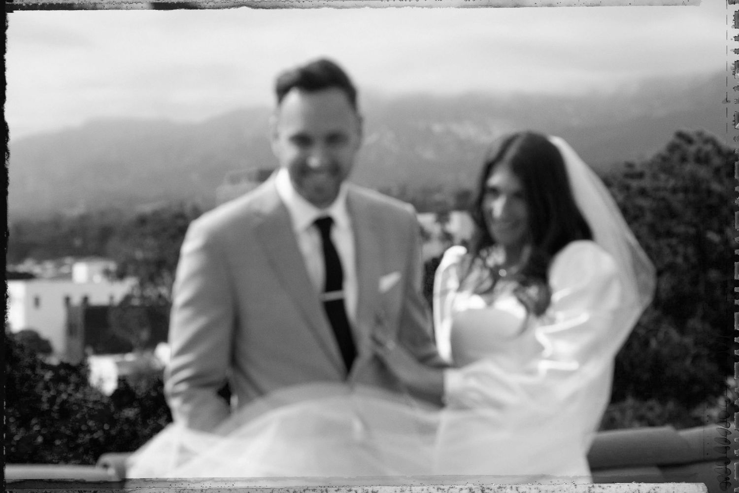 Black and white wedding photo of smiling bride and groom outdoors with mountain backdrop.