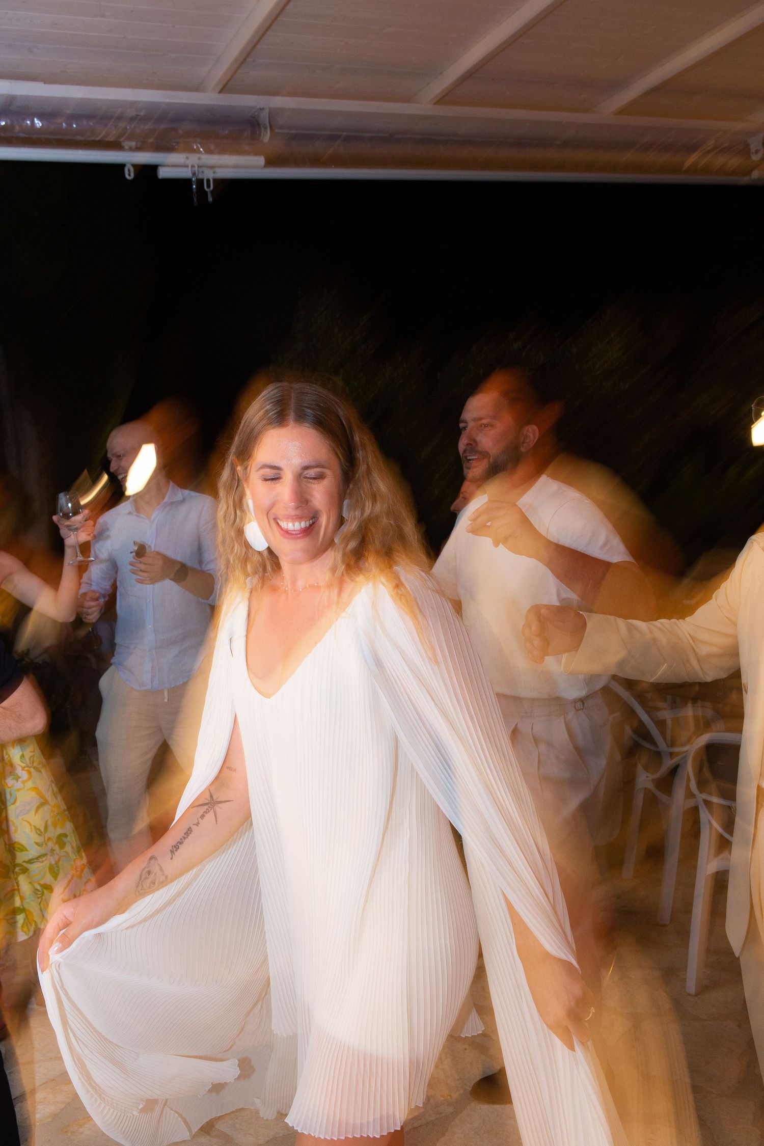 People in white outfits dancing and celebrating at a party in a dimly lit venue.
