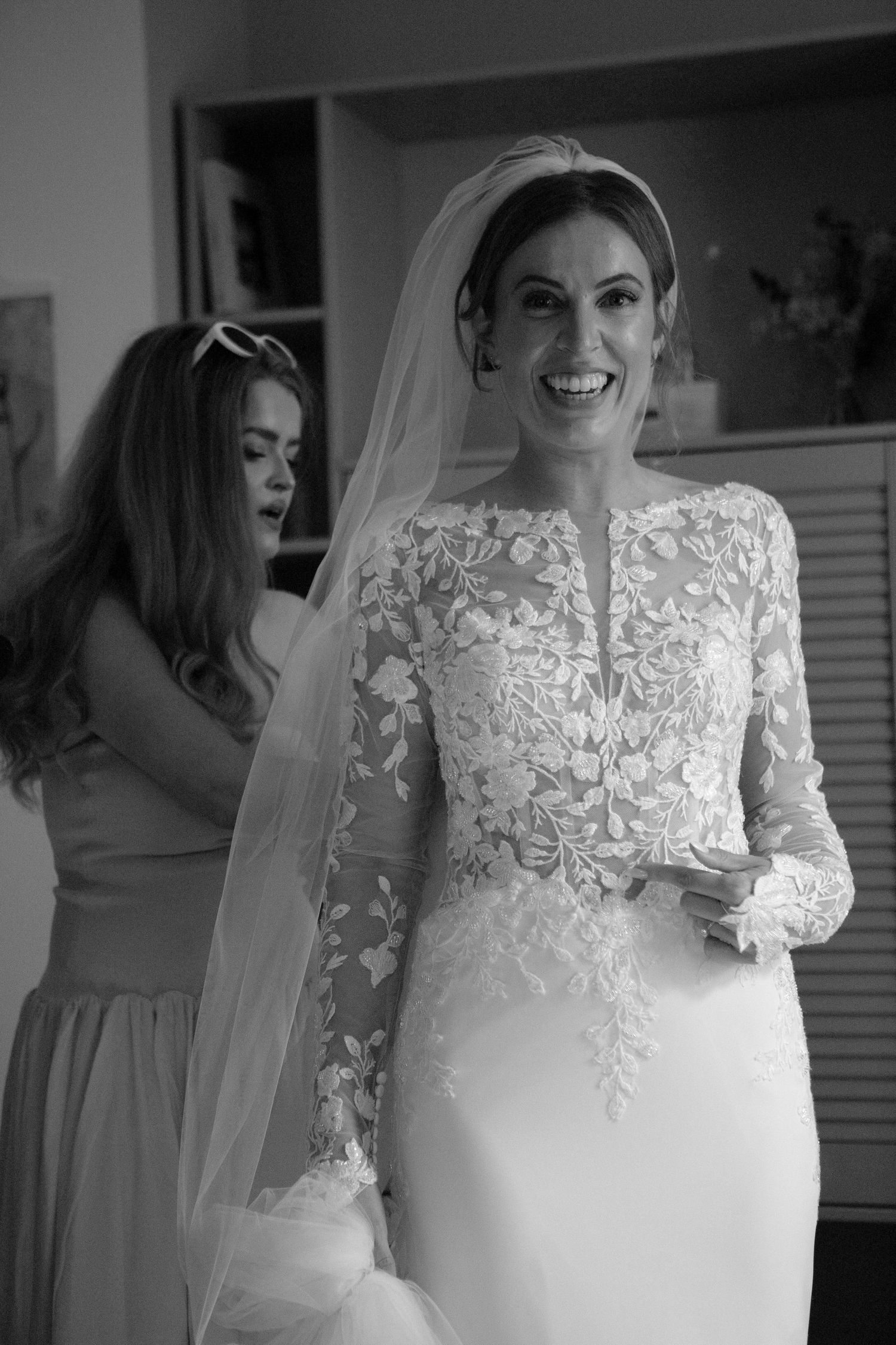 A black and white wedding photo series showing details of a lace bridal gown and veil during preparation moments.