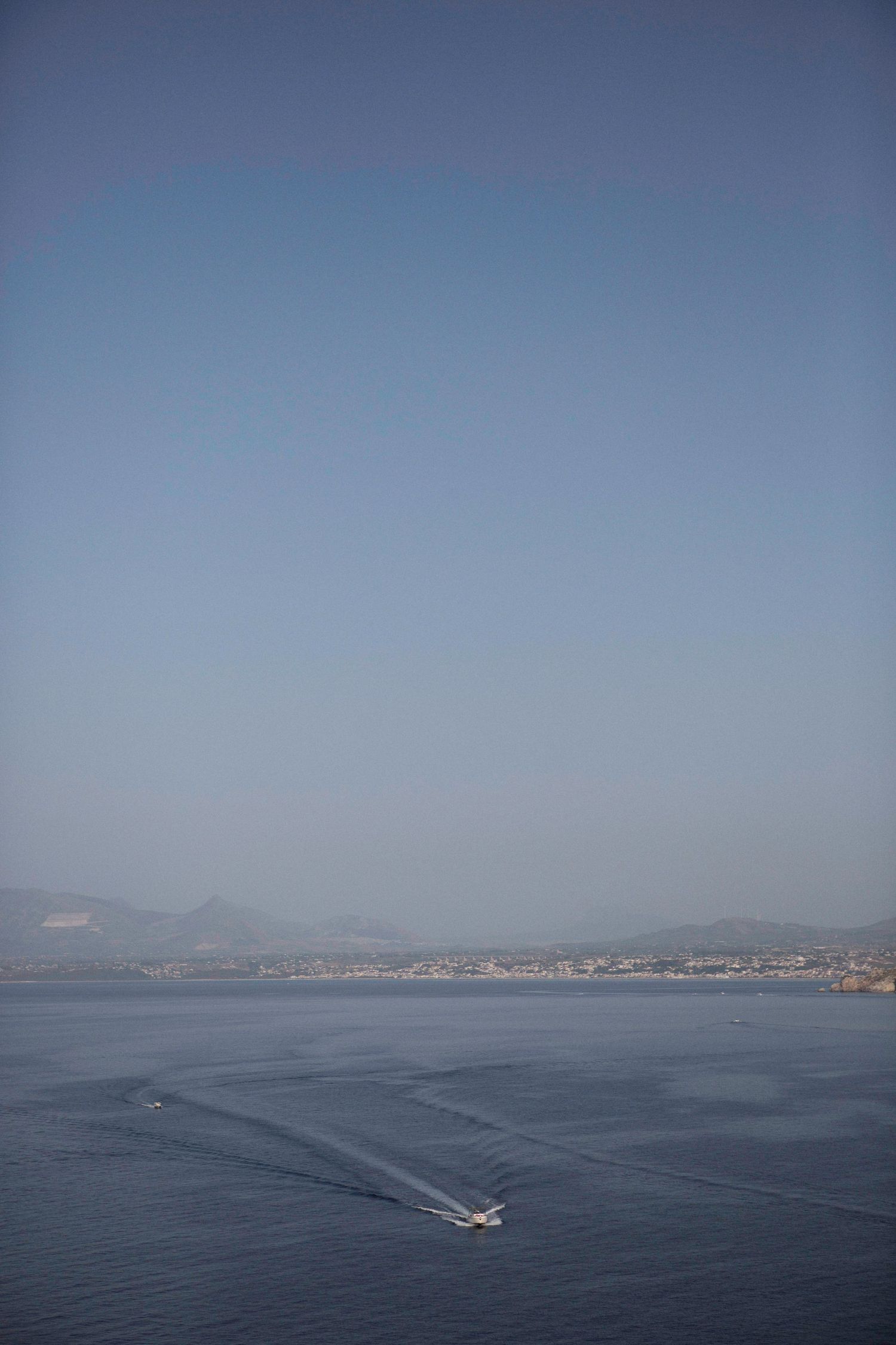 A panoramic sequence shows a small boat creating a wake trail across a misty blue ocean with distant coastal mountains.