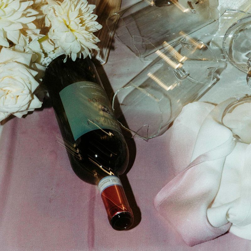 A wine bottle lying on a pink tablecloth beside white flowers and elegant glassware at a formal event.