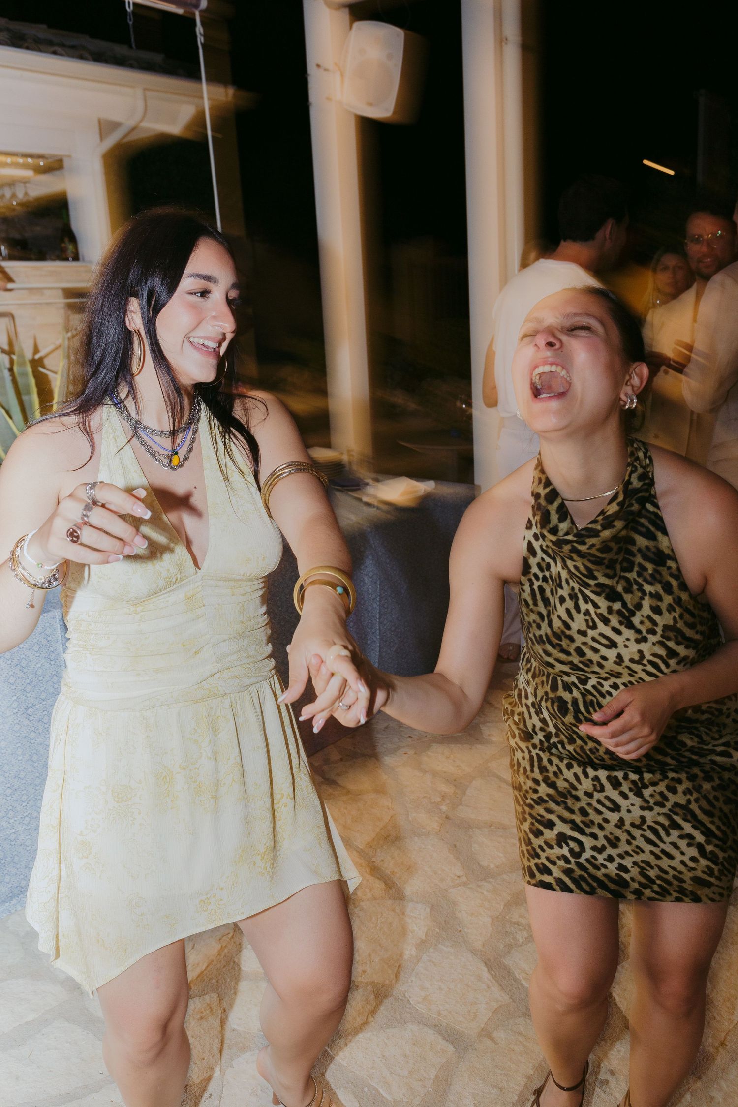 Two friends dancing and having fun at a party, one wearing a white dress and one in a leopard print dress.