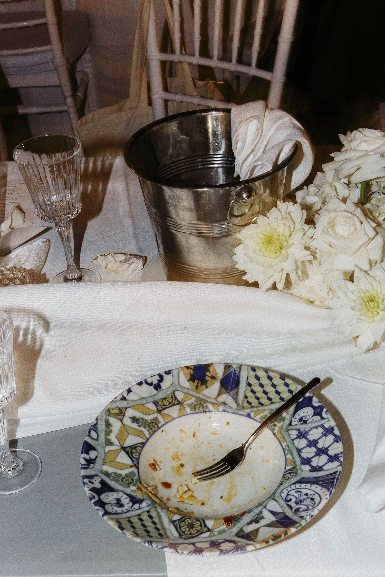 Used decorative plates with blue and gold patterns sit on a white tablecloth next to white floral centerpieces.