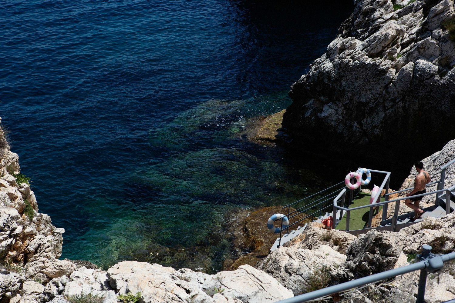 Rugged Mediterranean coastline with crystal clear turquoise waters and white limestone cliffs under bright sunlight.