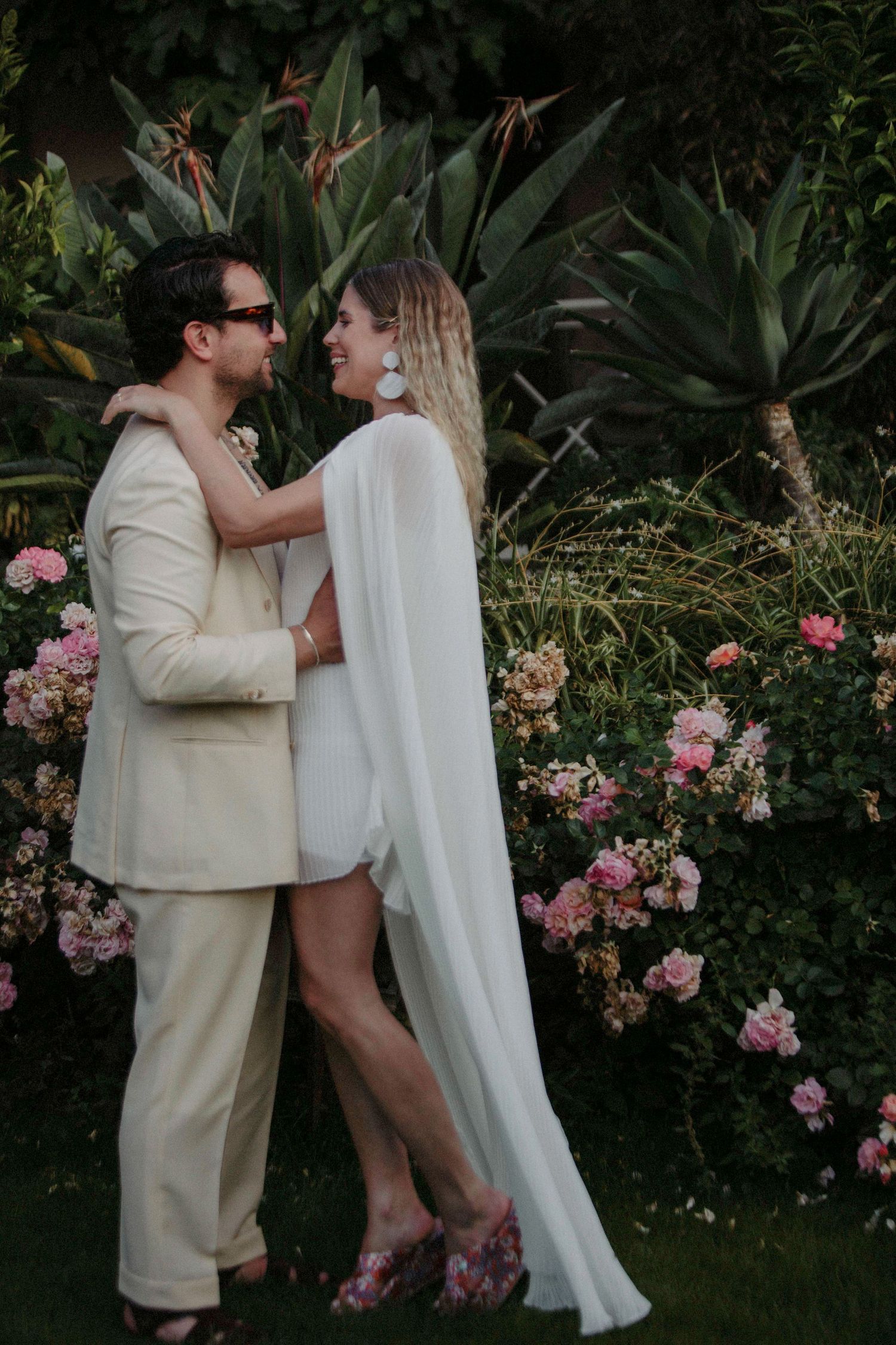 A romantic moment shared between a couple in front of blooming pink roses in a garden setting.
