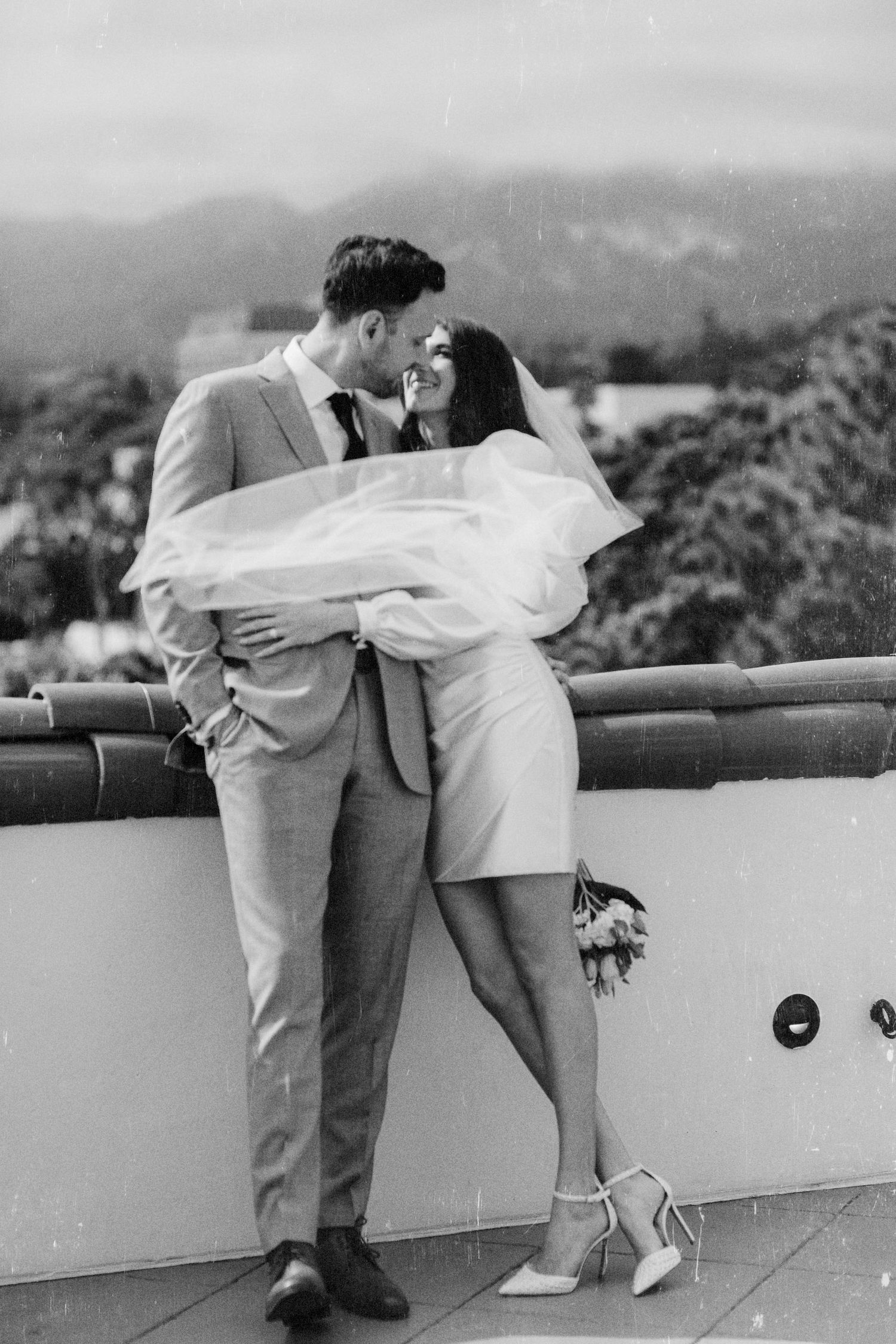 A sequence of black and white photos showing a couple in white clothing leaning over a balcony railing in a romantic pose.