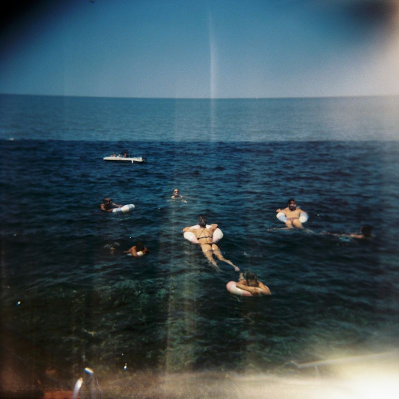 Vintage photo of swimmers and surfers enjoying a summer day in deep blue ocean waters.