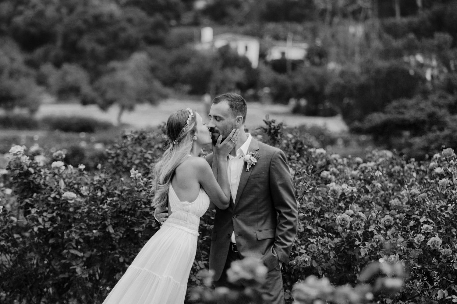 A romantic wedding couple embraces among lush garden greenery during their outdoor celebration.