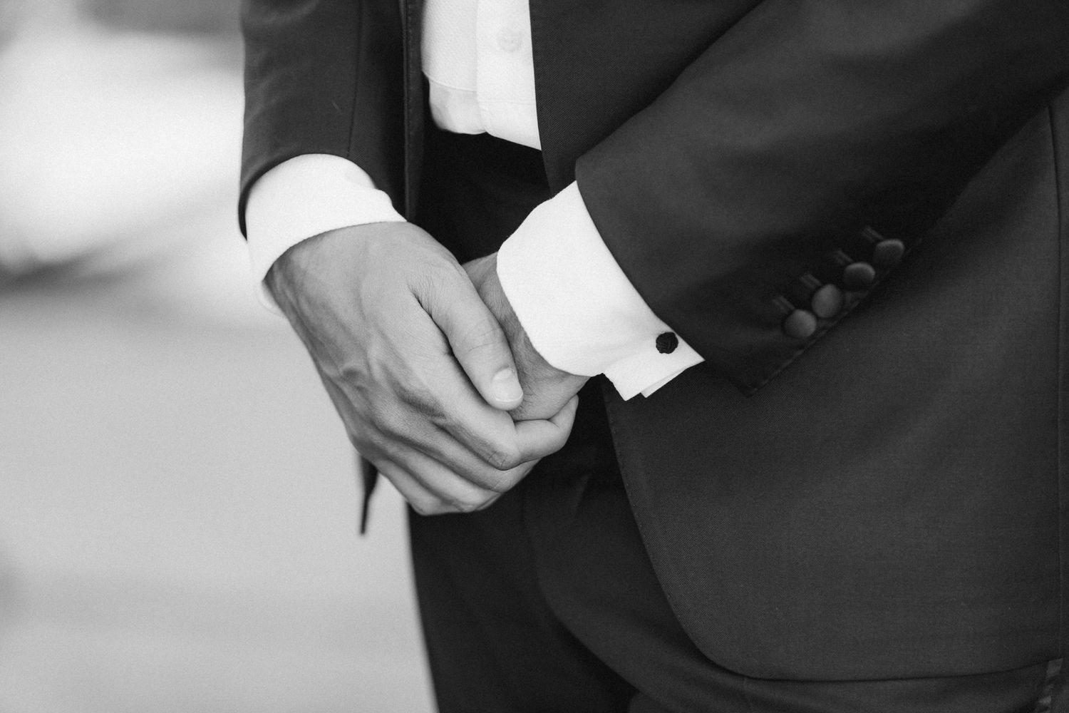 Black and white close-up of hands adjusting formal suit cuff links and white dress shirt sleeve.