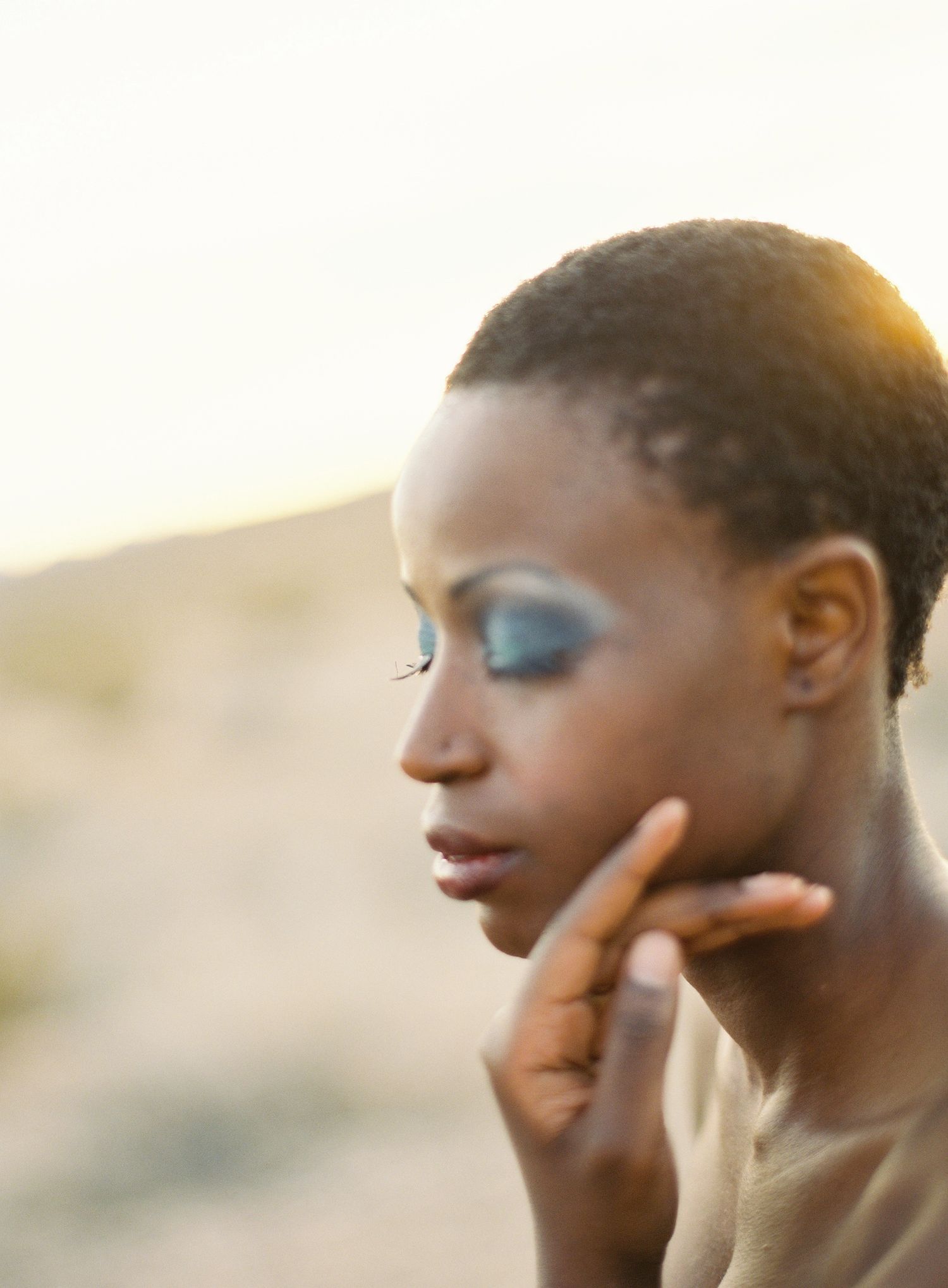 Five artistic profile portraits showing dramatic eye makeup and metallic skin tones against a warm sunset backdrop.