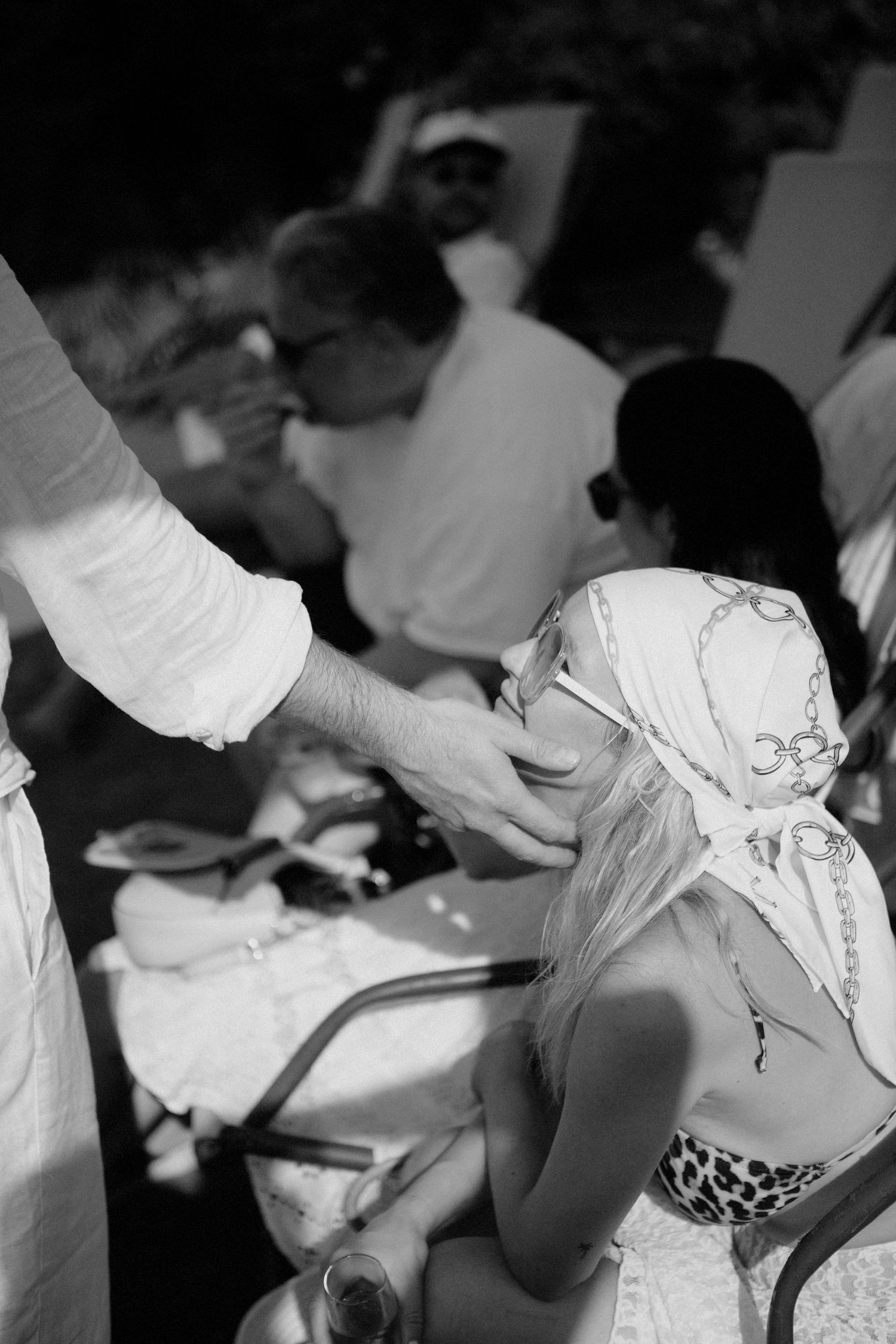 Black and white photo of a woman in a headscarf and sunglasses at an outdoor gathering.