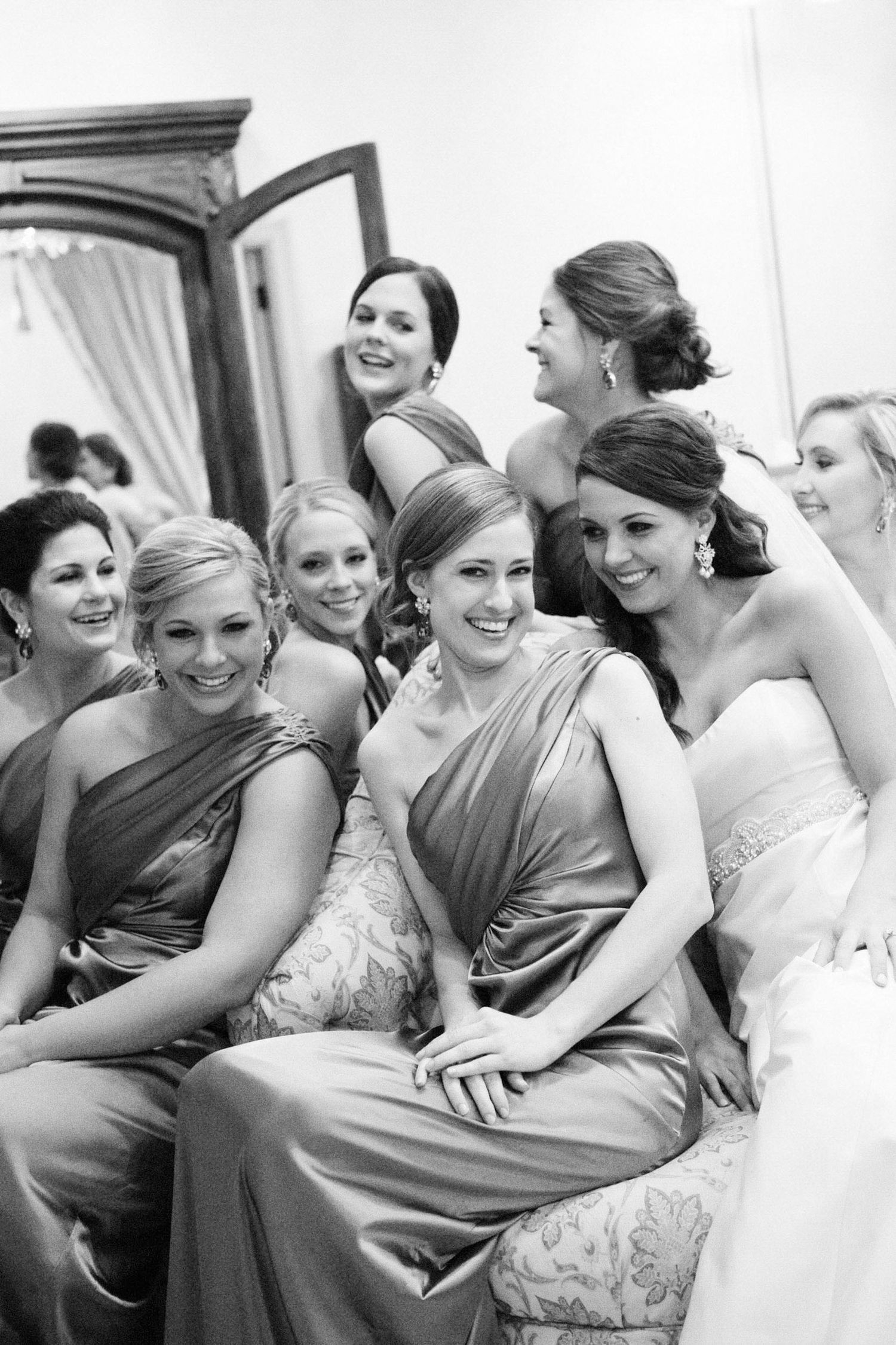 Black and white photo of a bride with her bridesmaids in elegant gowns, smiling together at a wedding celebration.