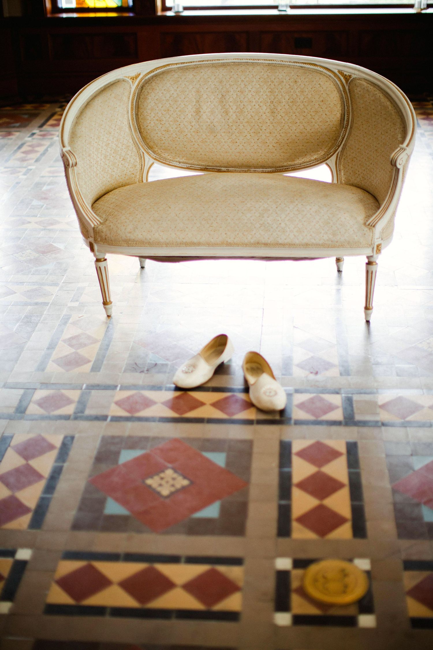 Antique cream-colored settee photographed from different angles on a geometric patterned floor with diamond shapes.