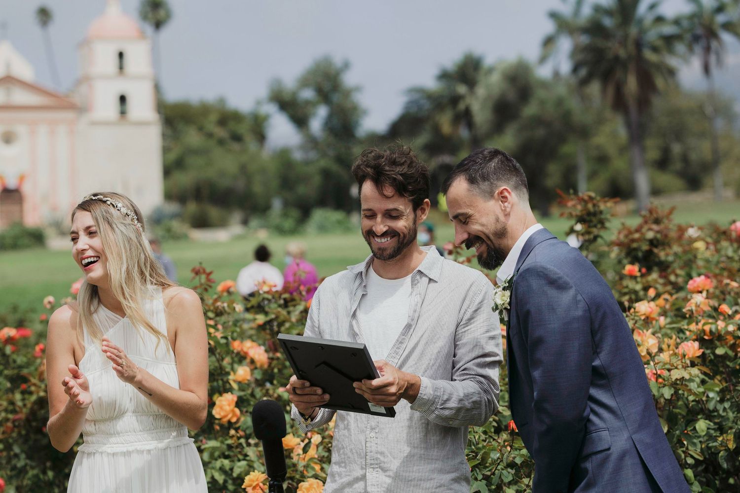 A couple shares joyful moments in a lush garden filled with blooming flowers and palm trees on a sunny day.
