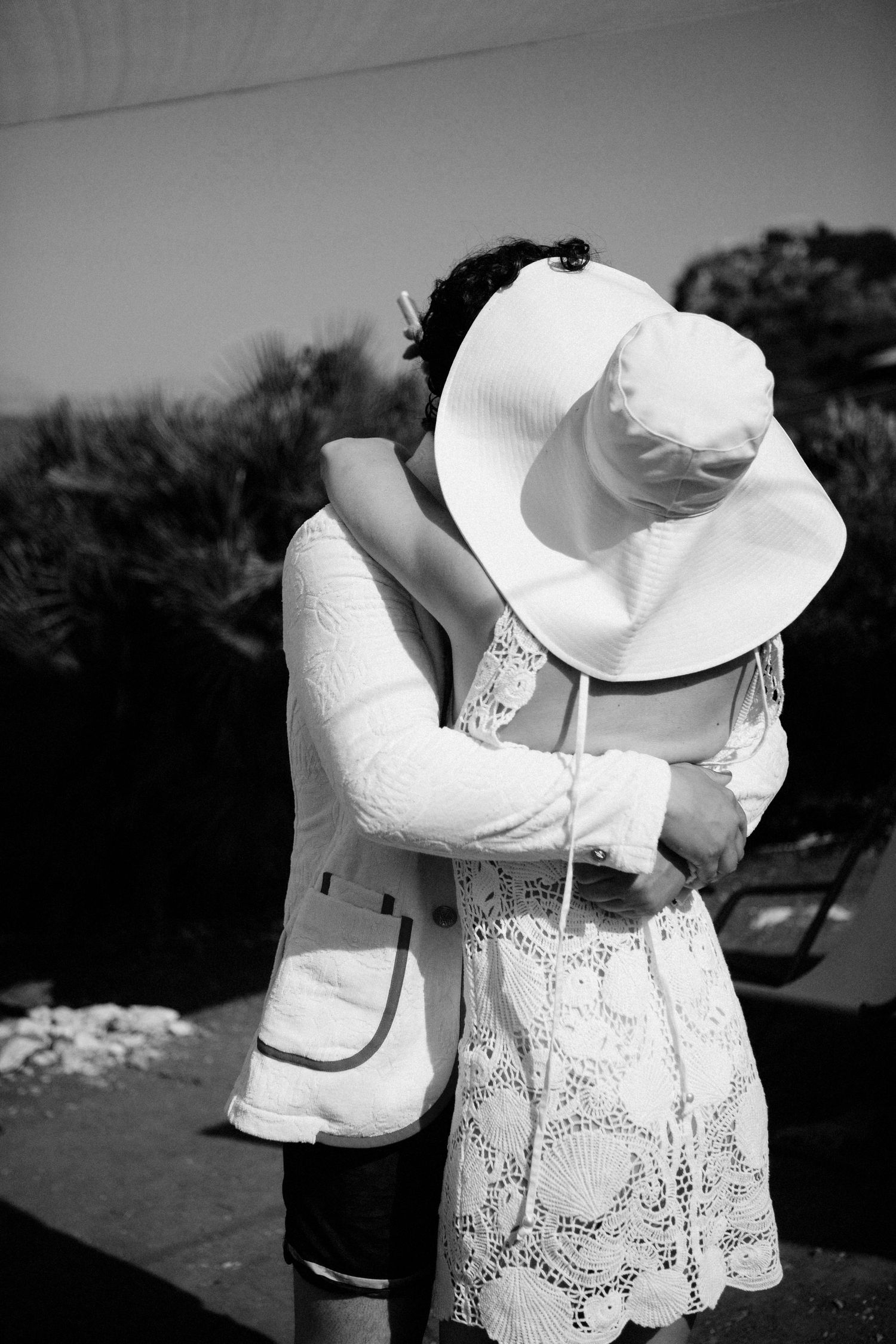 A romantic black and white photo shows a couple embracing, with one wearing a white lace dress and large sun hat.