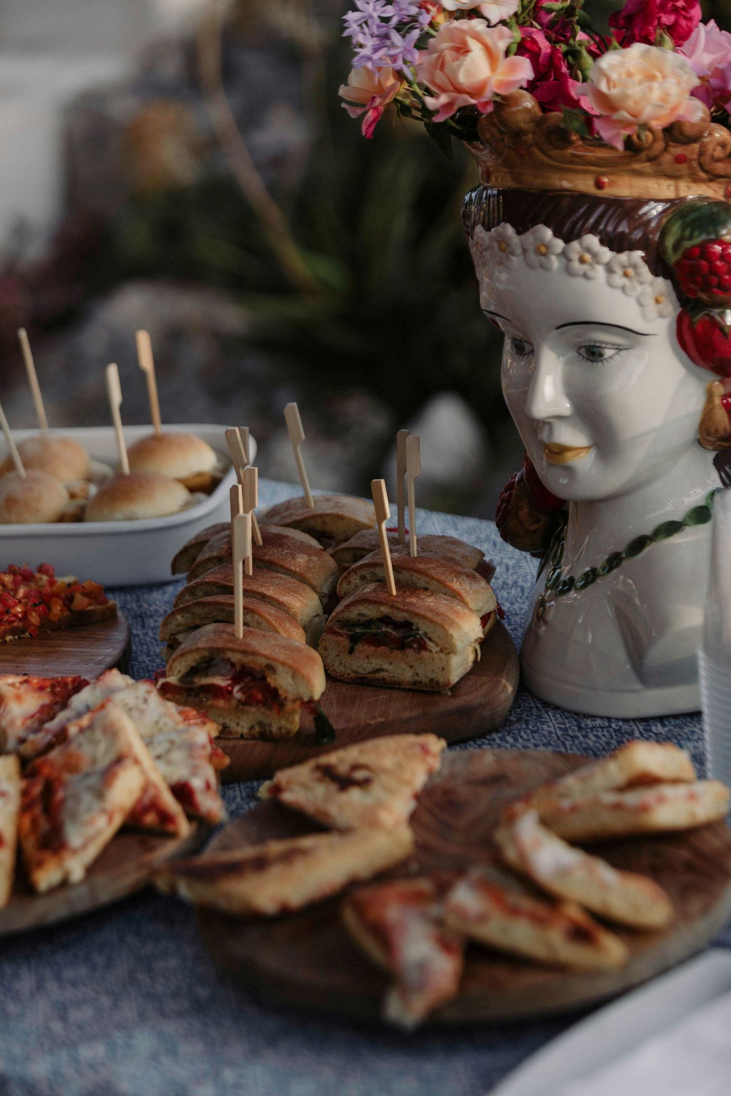 Rustic wooden boards display an assortment of sliced sandwiches with decorative floral arrangements in the background.