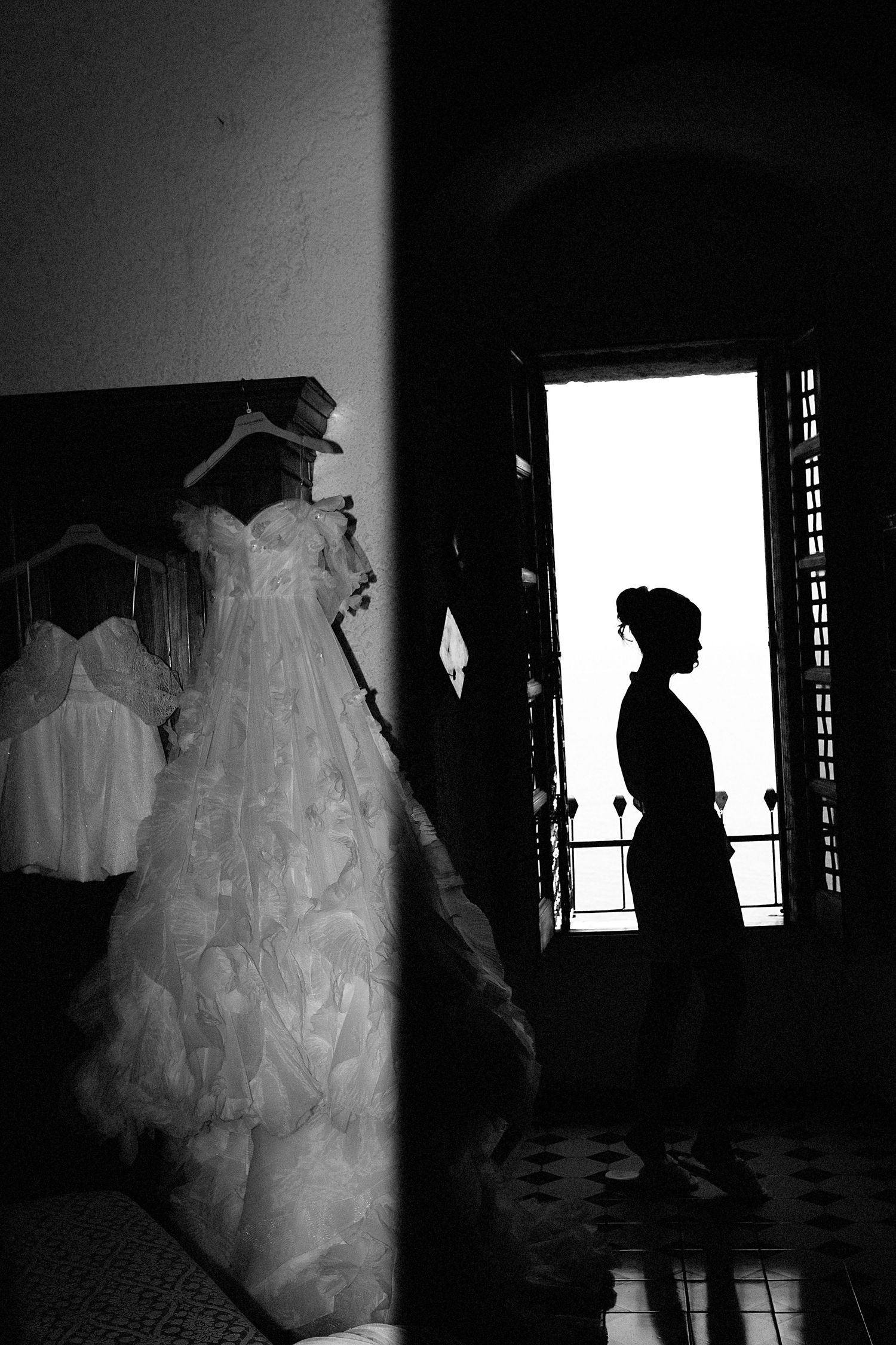A dramatic black and white photo series shows silhouettes against windows with wedding dresses in a dark room.