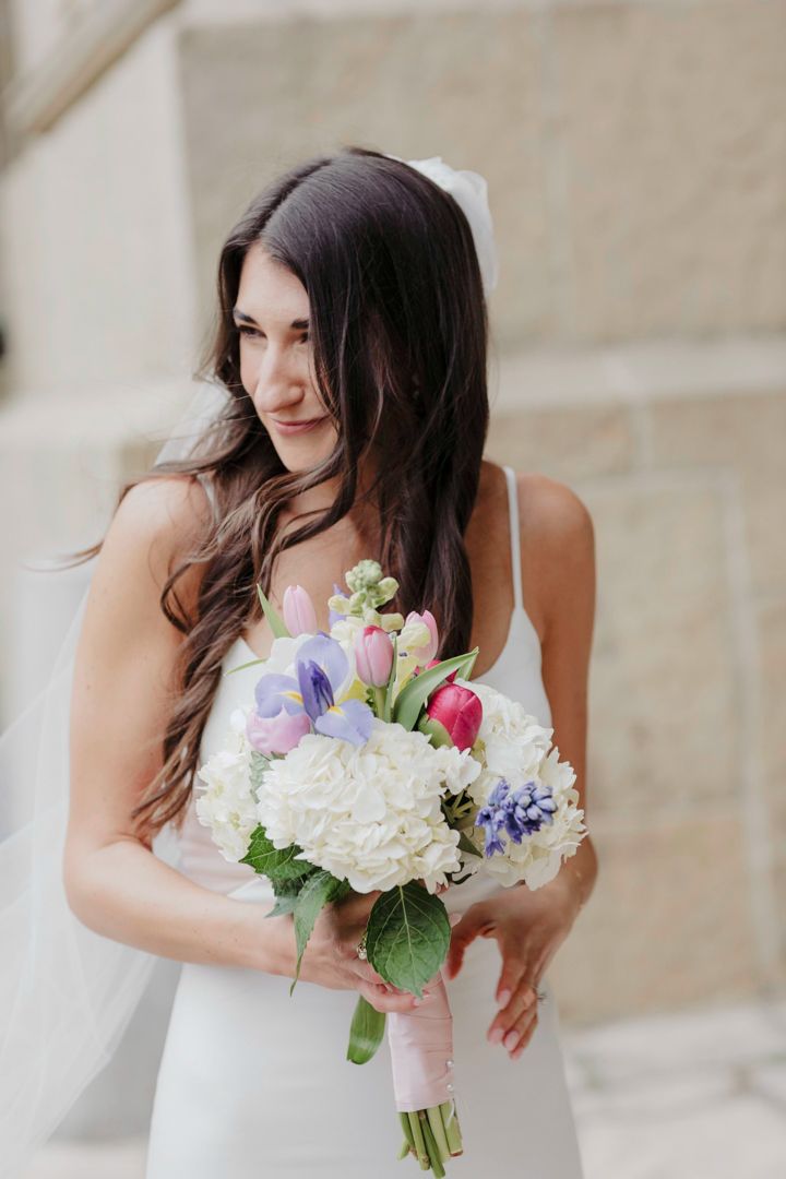 A wedding bouquet with white hydrangeas and purple flowers is held against a white dress in a series of detail shots.