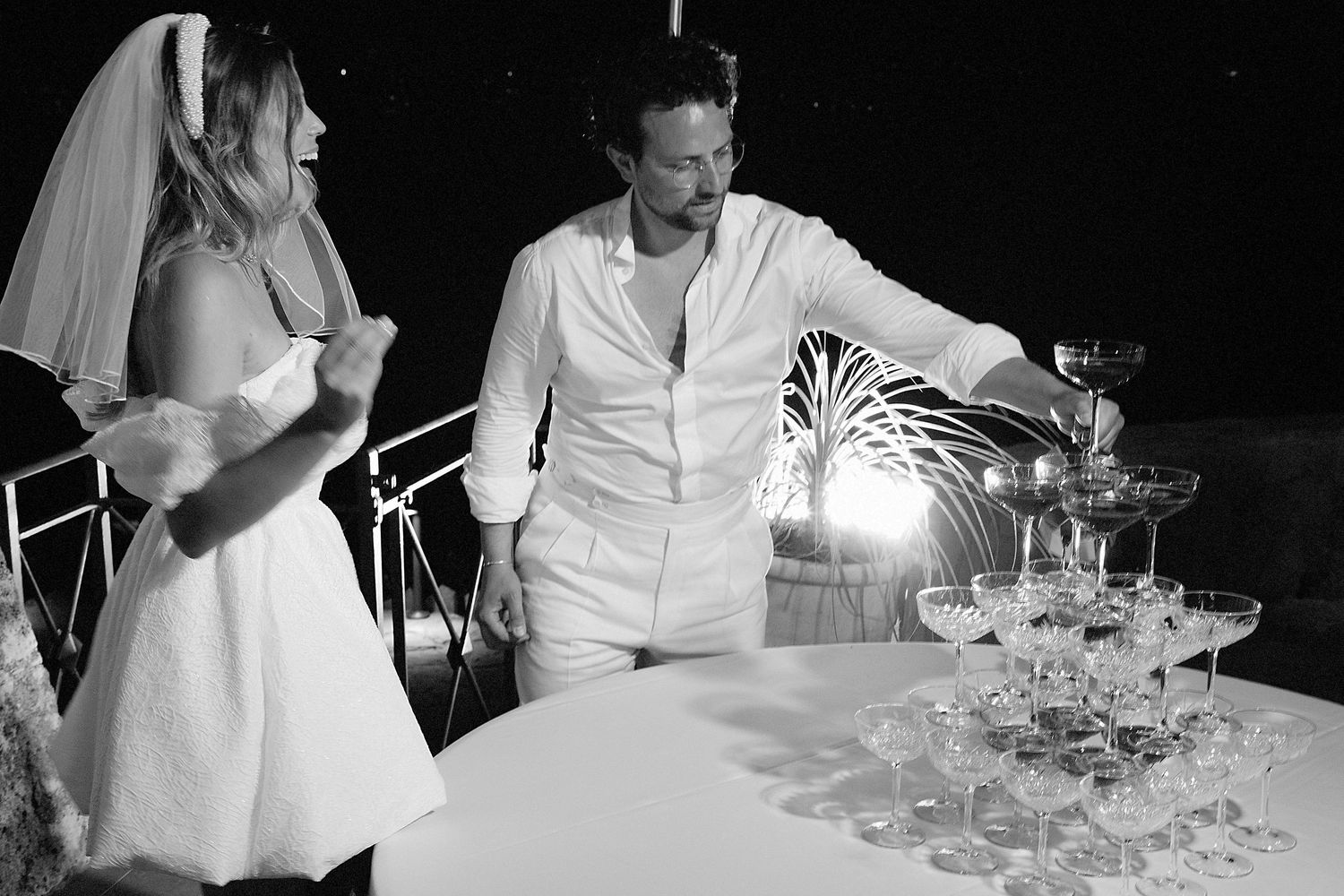 A couple in white attire shares a romantic moment during a candlelit dinner at an elegant restaurant.