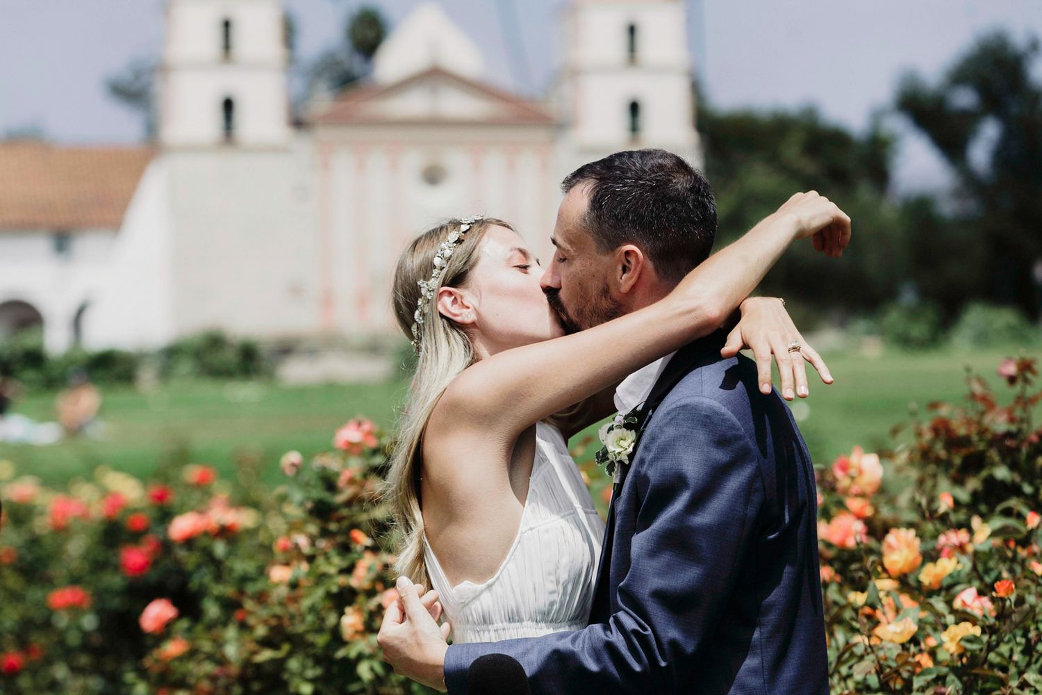 A romantic moment shared between a couple in front of Santa Barbara Mission with blooming roses in the foreground.