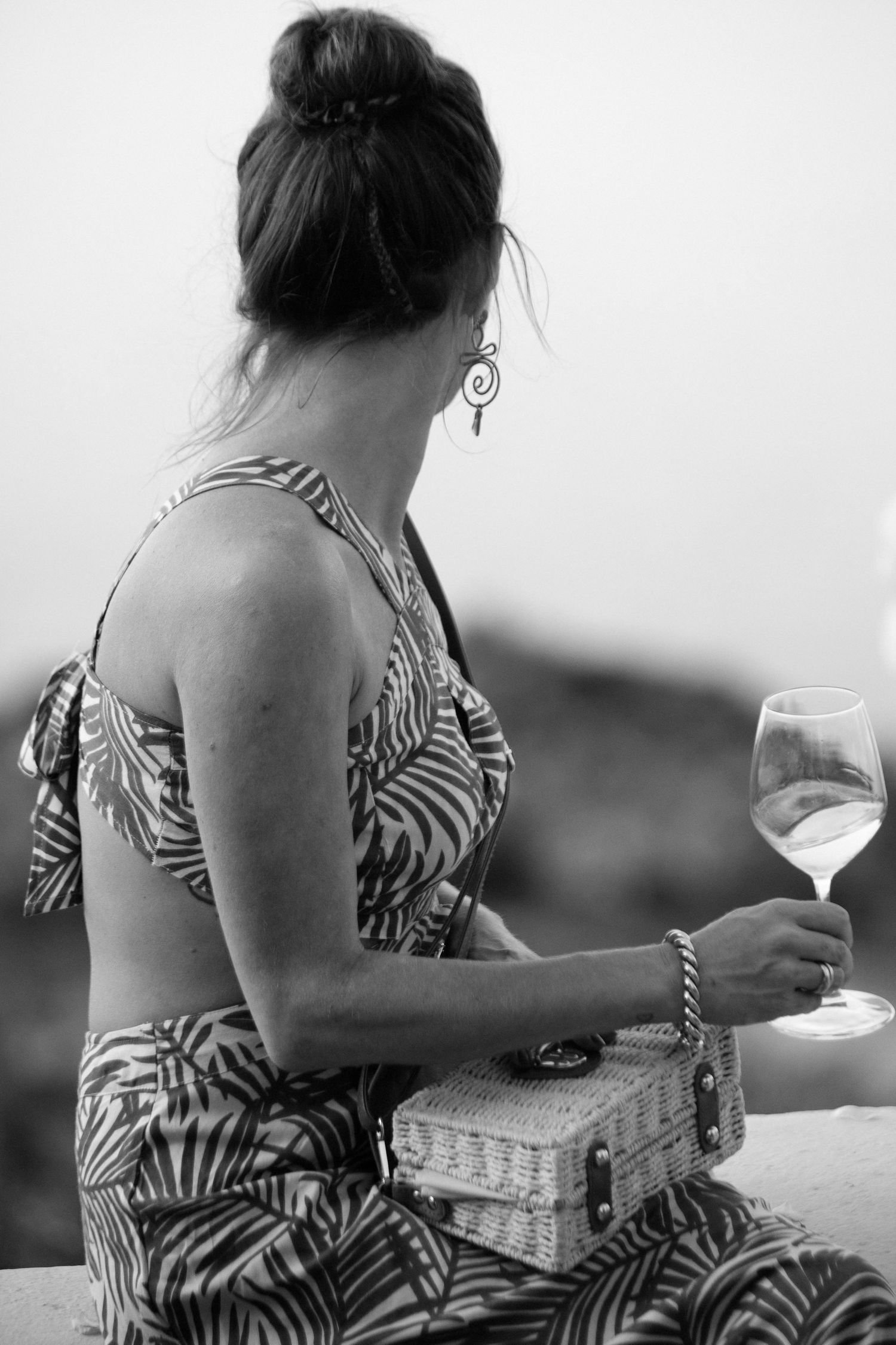 A person in a zebra print dress sits outdoors with a glass of white wine in a black and white photo series.